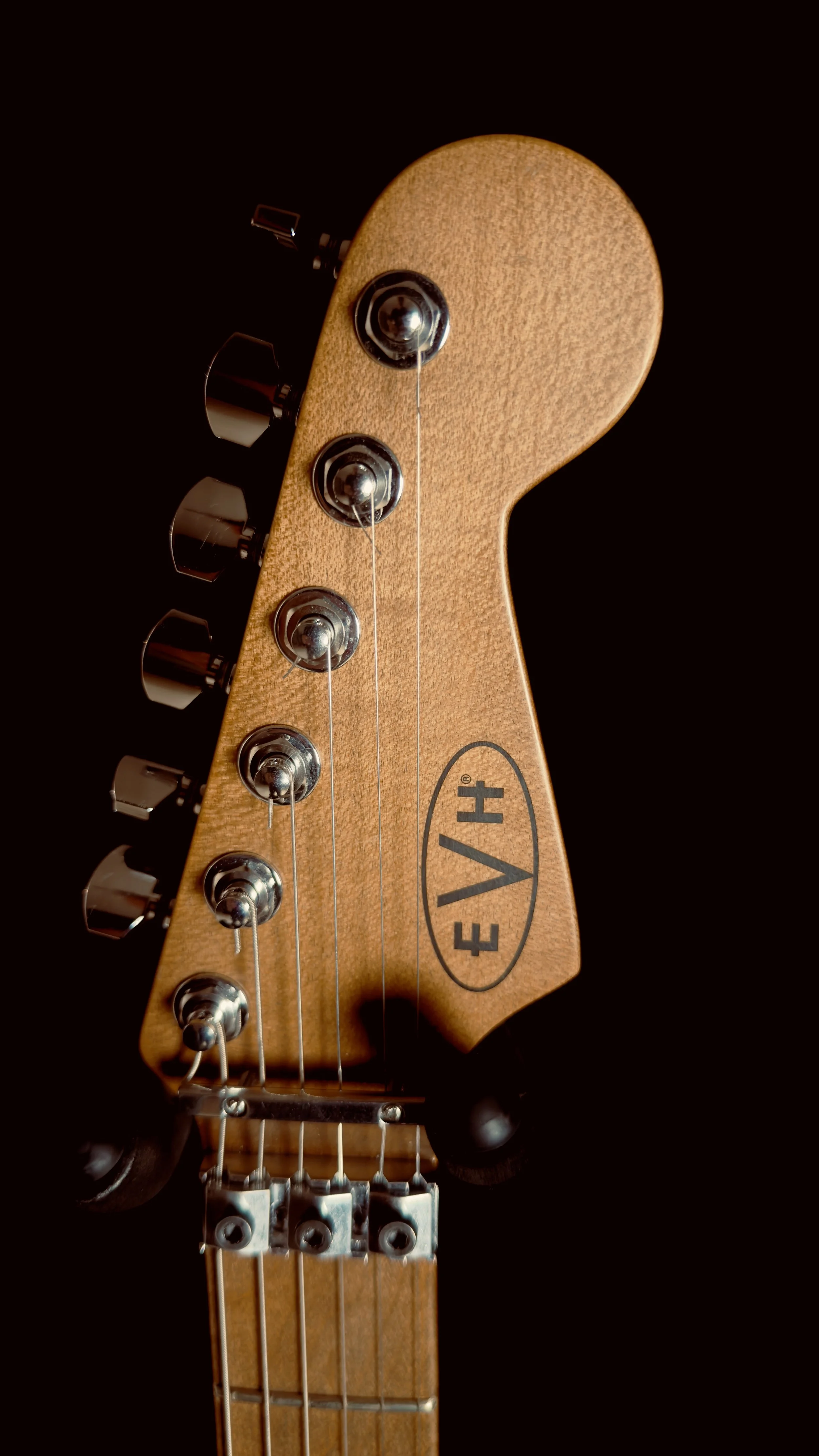 Close-up of an EVH guitar headstock with tuning pegs and strings, isolated on a black background.