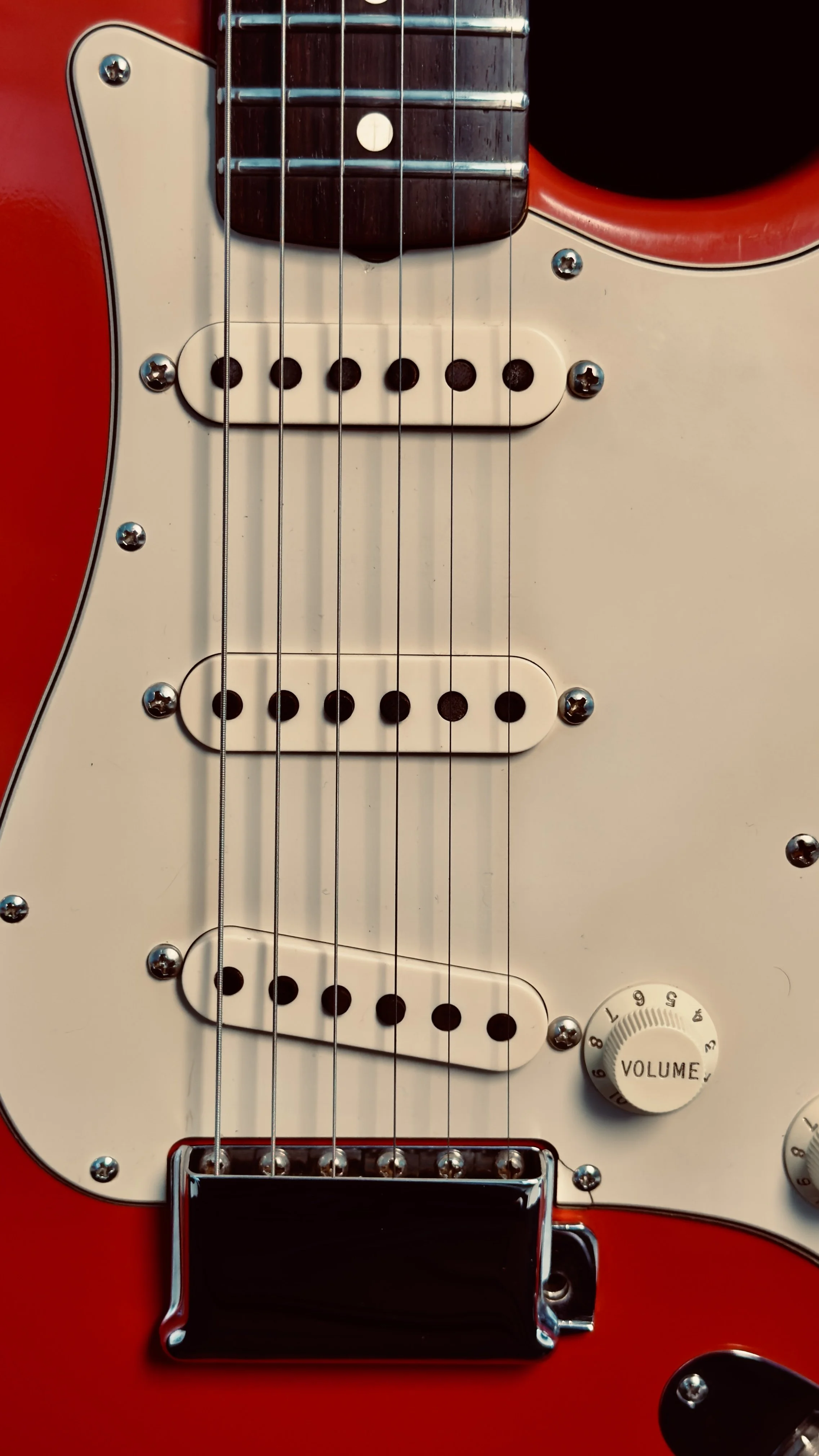 Close-up of the body of an electric guitar, featuring strings, pickups, volume knob, and a red and white finish.