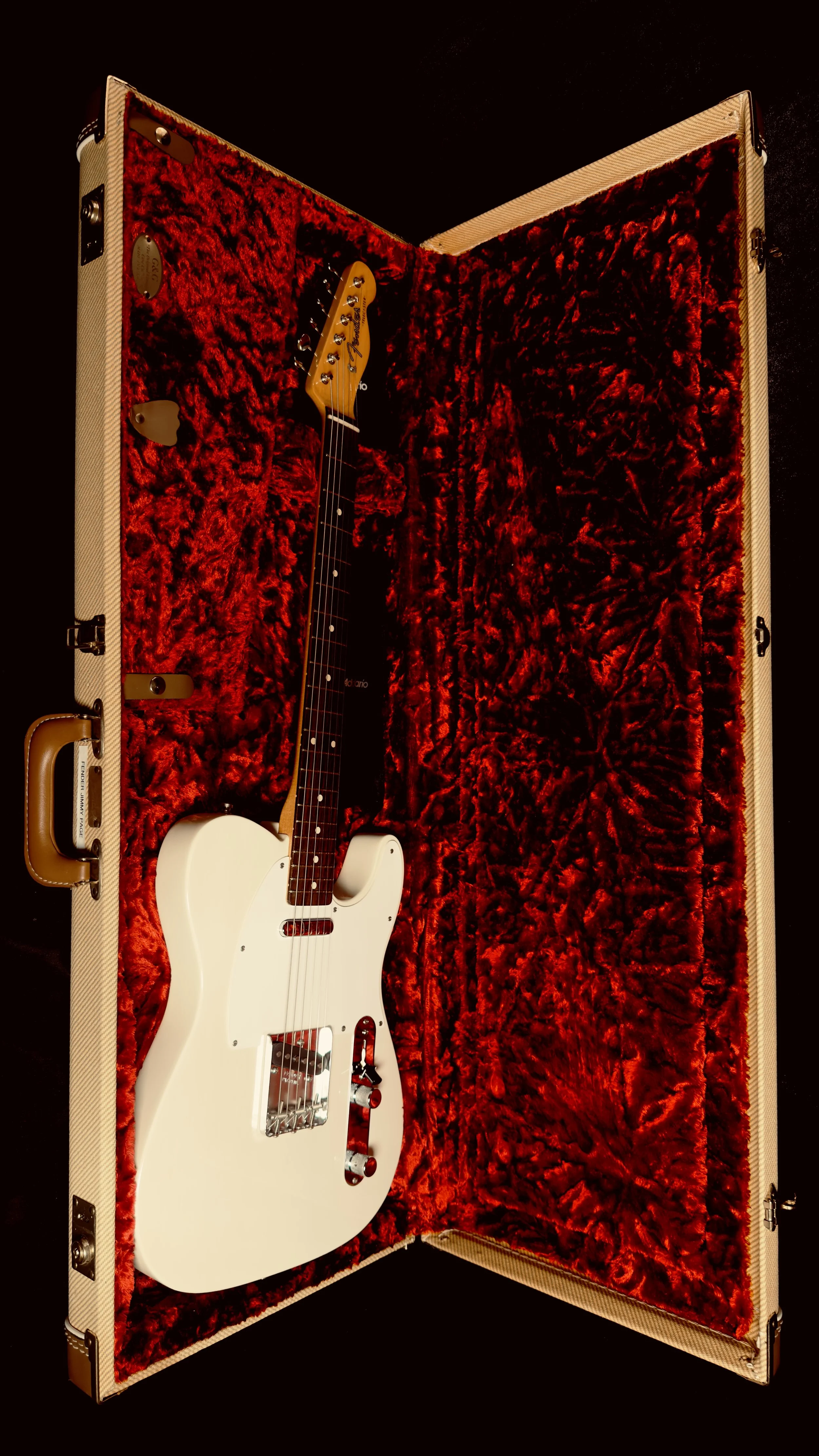 A white electric guitar inside a beige hard case lined with red plush fabric.