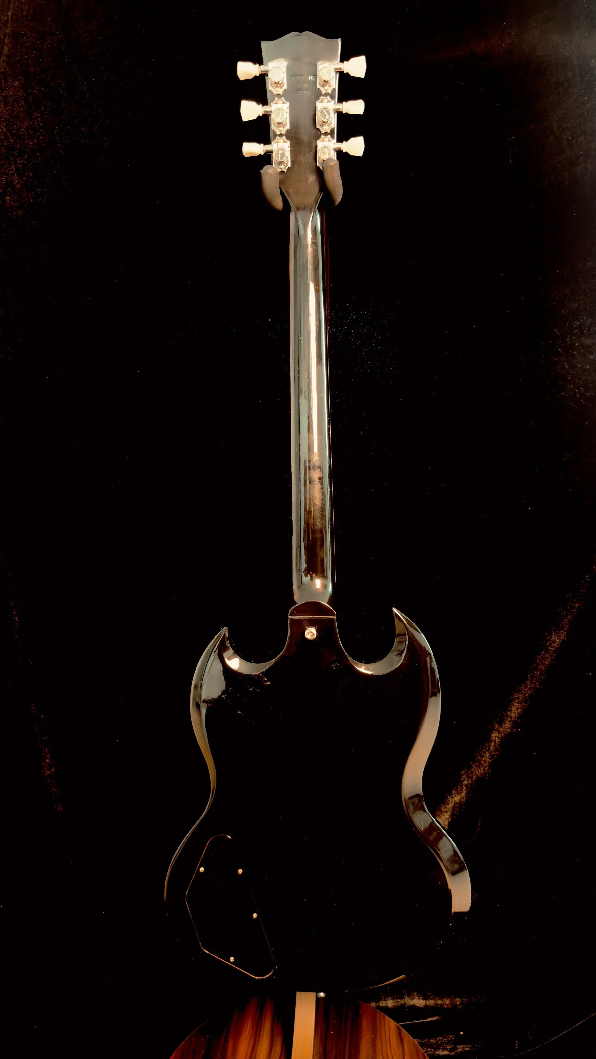 Back of an electric guitar with chrome hardware, against a black background.