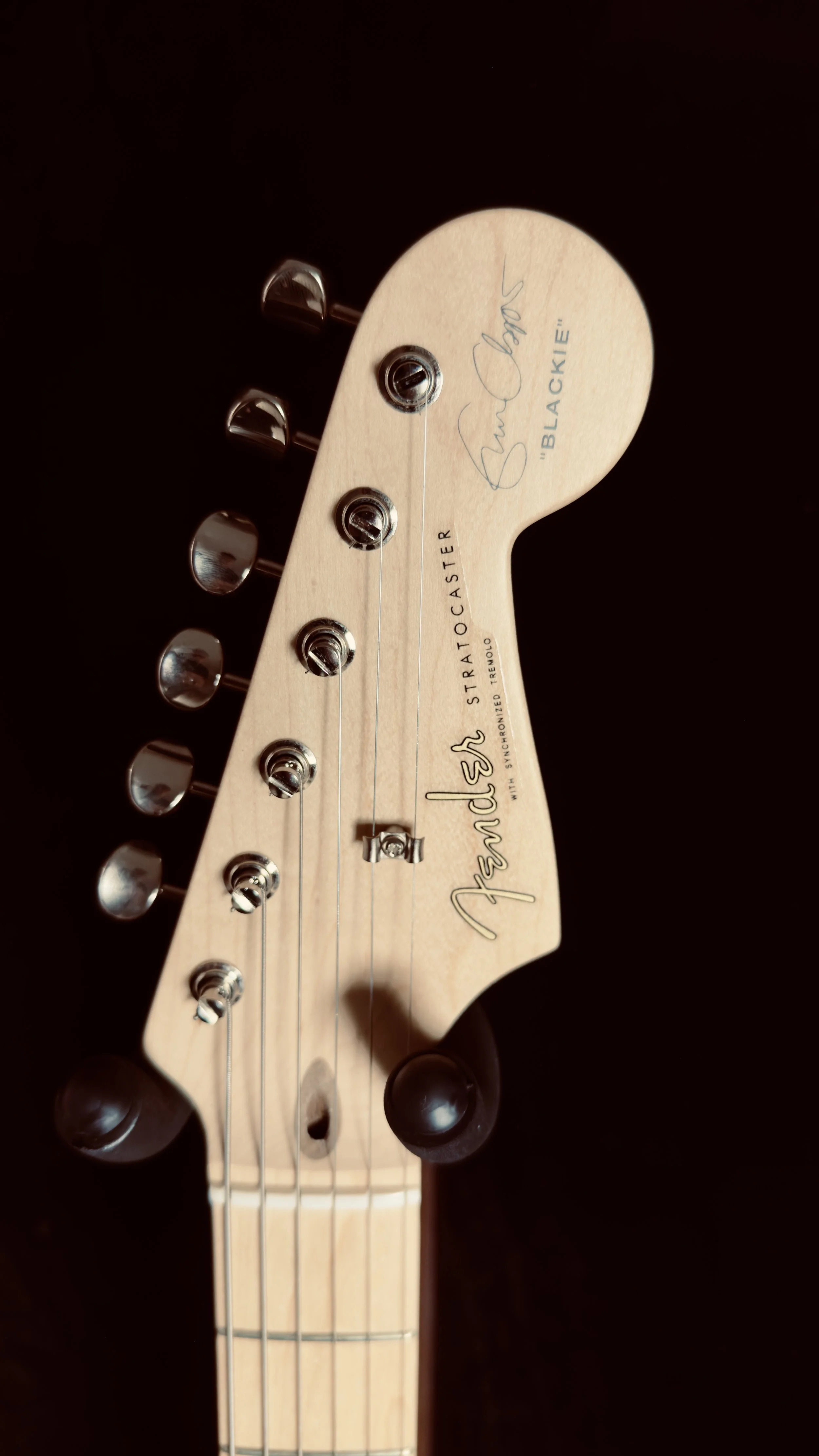 Close-up of a Fender Stratocaster guitar headstock with signature and label, set against a black background.