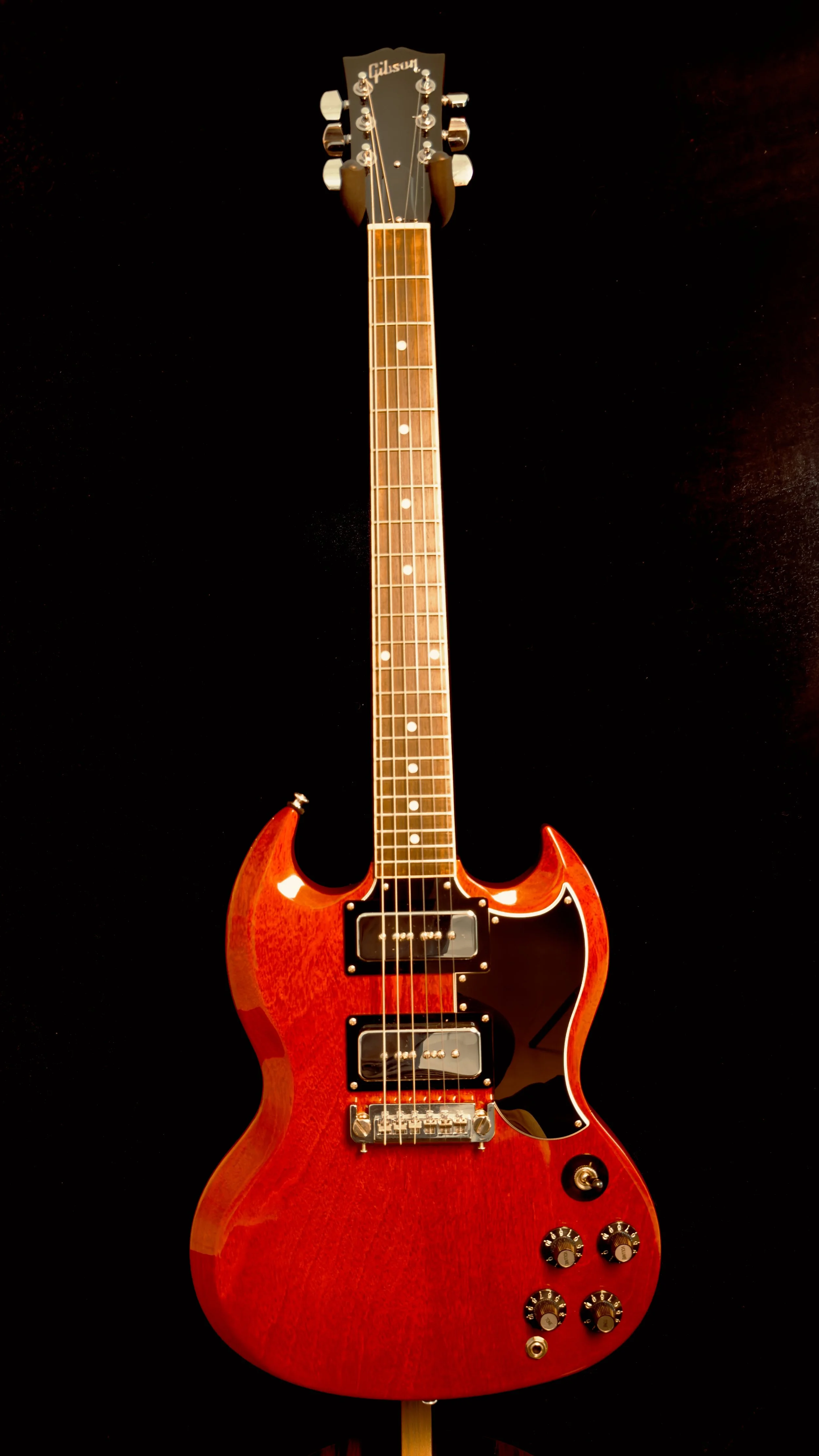 A red Gibson electric guitar with black pickguard, dual pickups, four control knobs, and a switch, set against a black background.