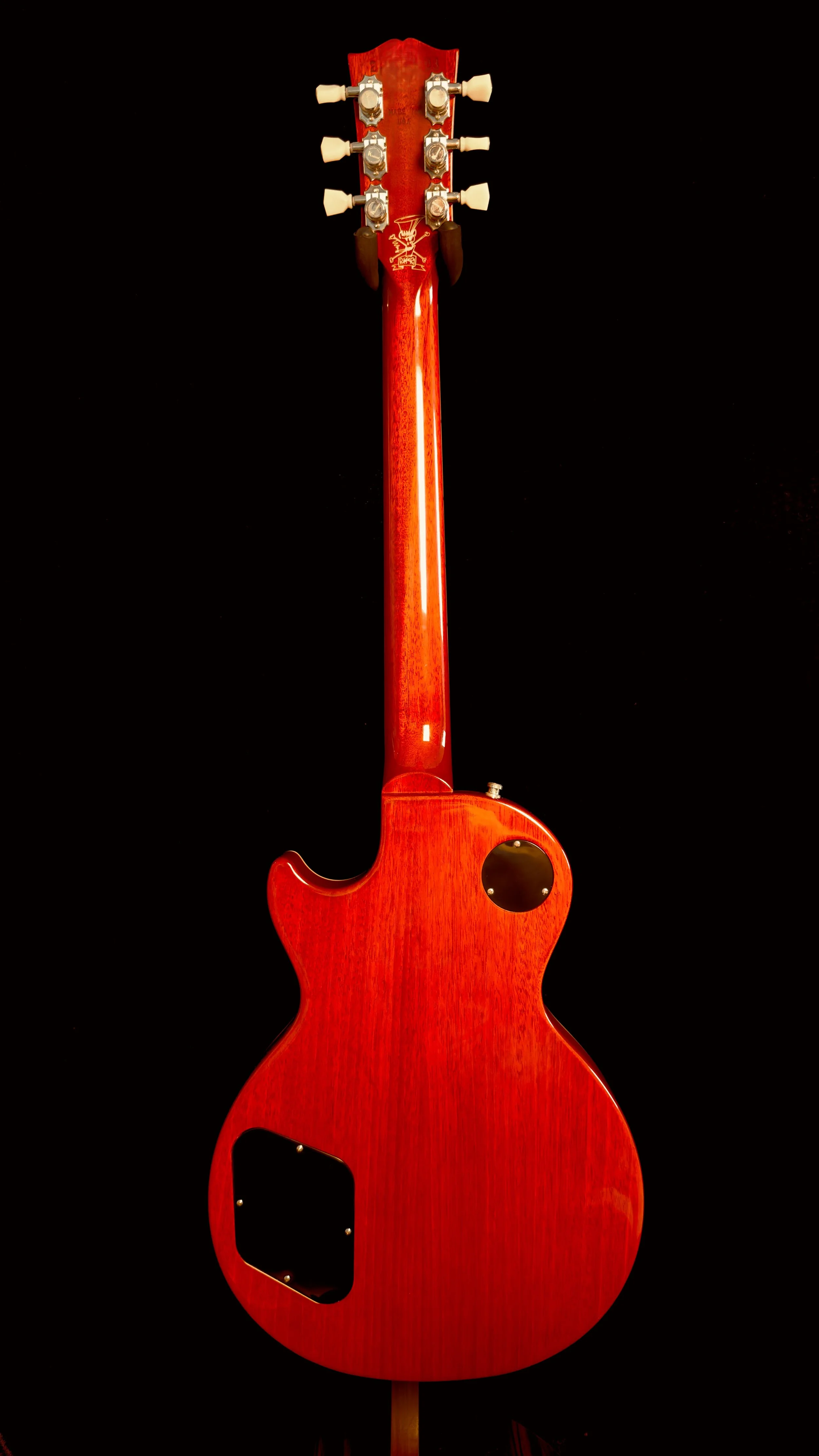 Back of a red electric guitar with tuning pegs, on a black background.