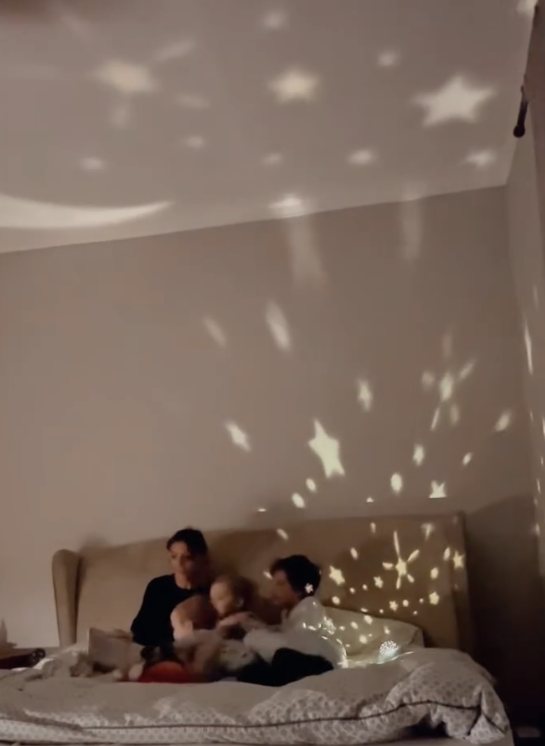 A family sitting on a bed with star-shaped light projections on the wall and ceiling.
