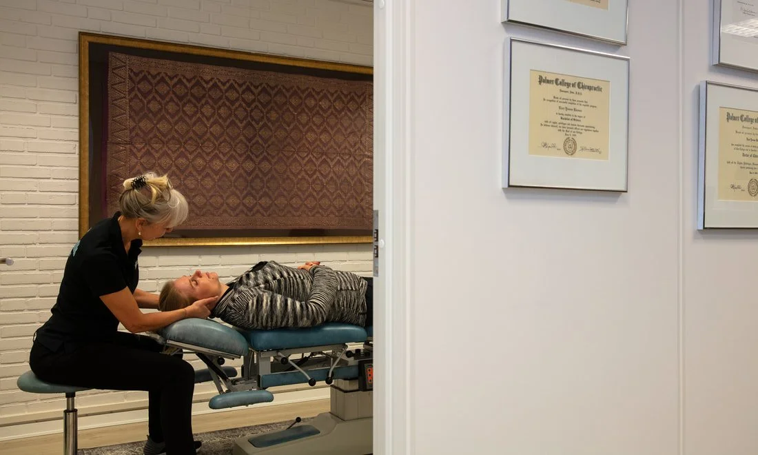 A healthcare provider performing a neck massage on a patient lying on a treatment table in a clinic or medical office.