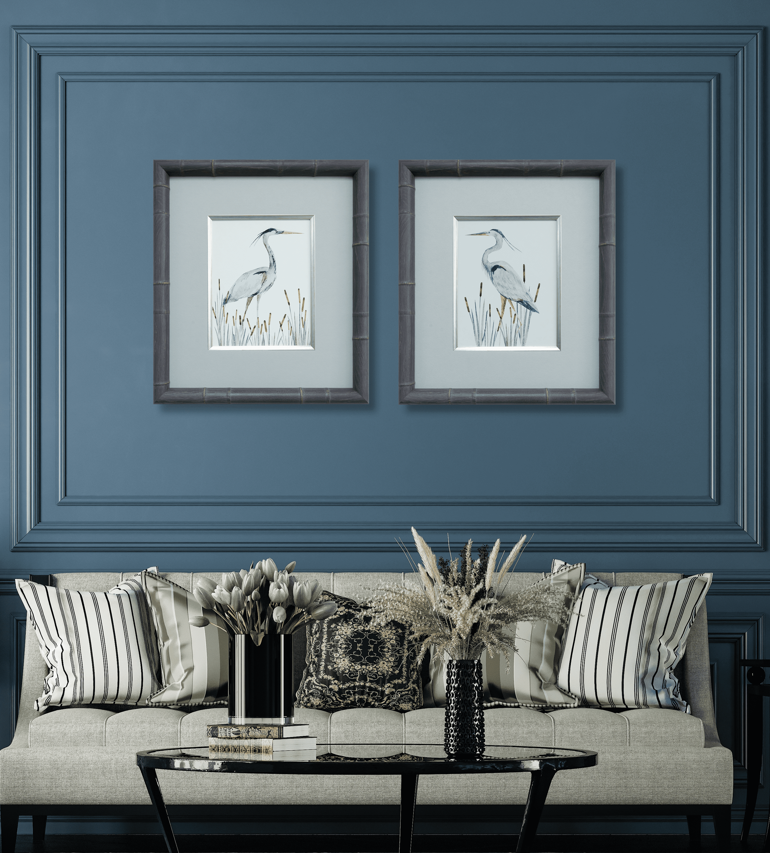 Living room with a light-colored sofa, striped throw pillows, a coffee table with books, two black vases with white and dried flowers, framed bird artwork on a blue wall, and decorative molding.