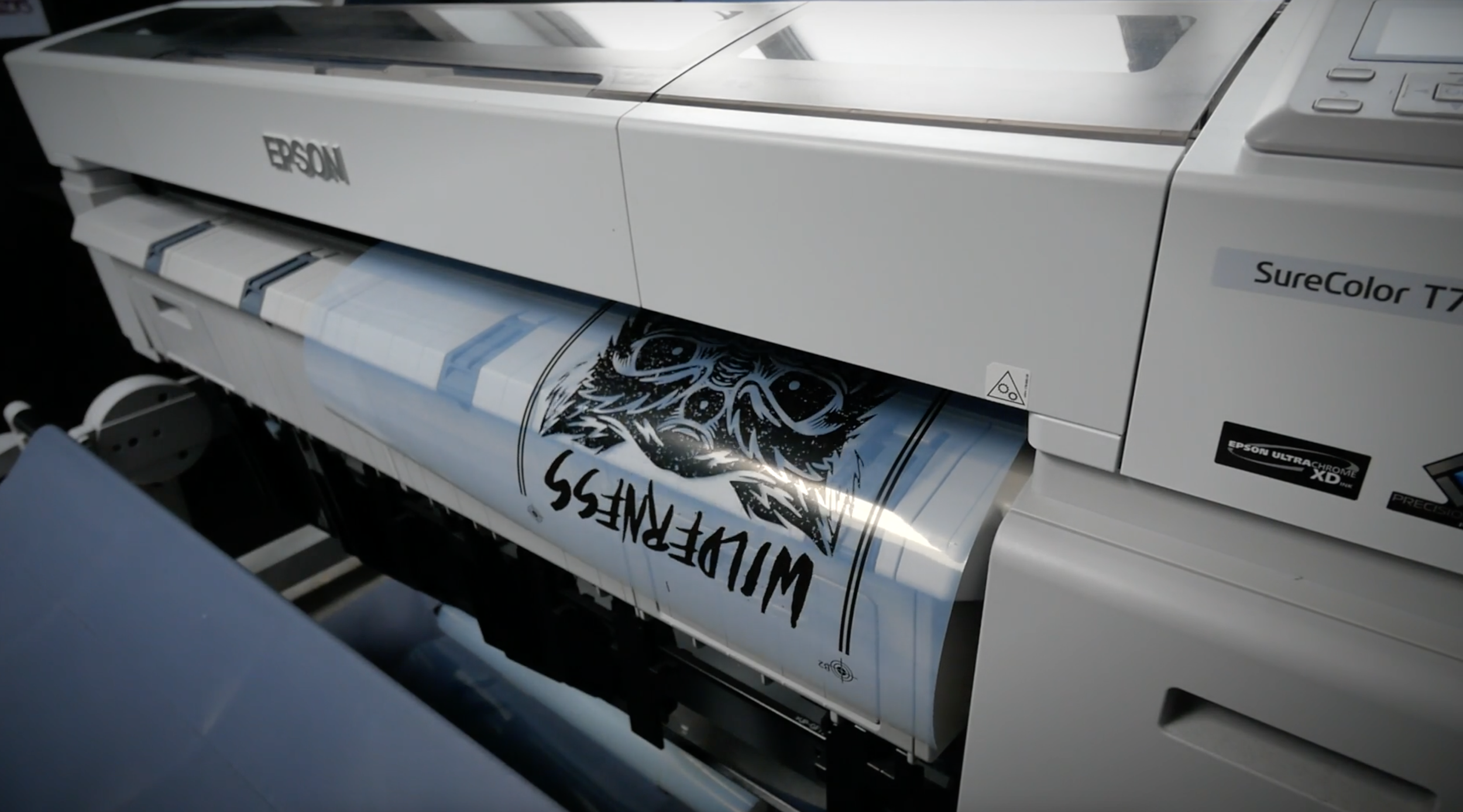 A large Epson printing machine printing a design with a wolf illustration and the word 'WILDERNESS' in bold letters.