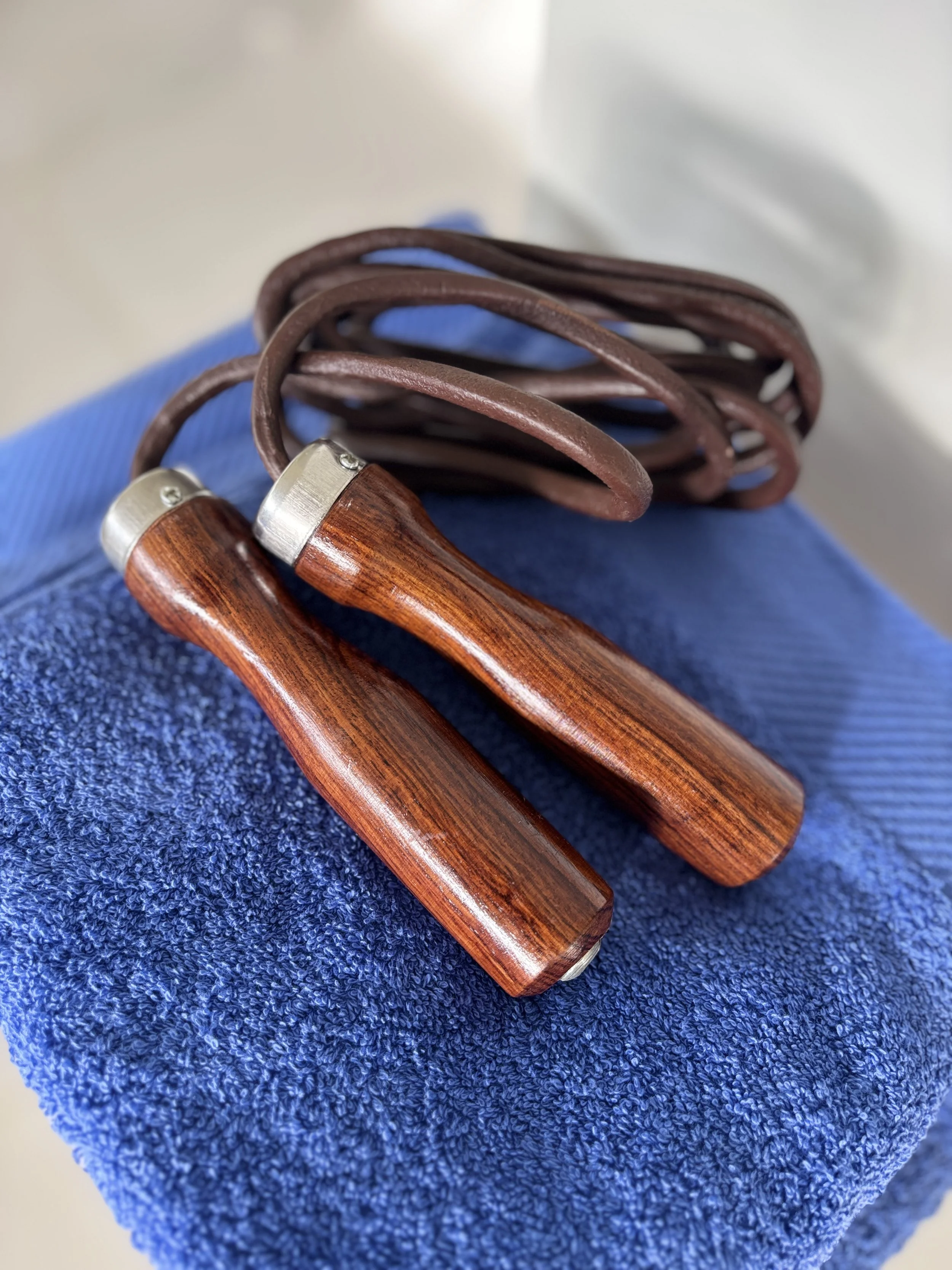 Une corde à sauter avec des poignées en bois reposant sur un tissu bleu.