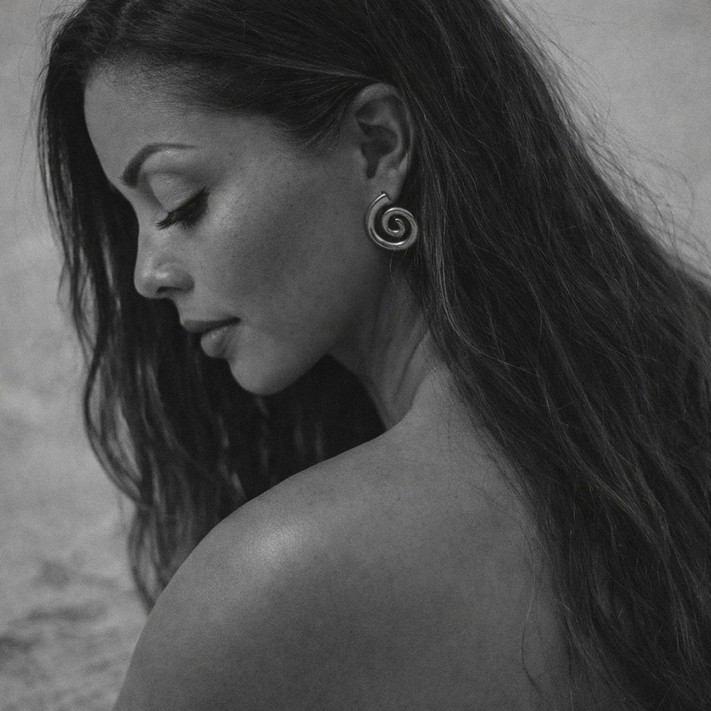 Close-up of a woman with long hair looking downward, wearing a spiral earring in her left ear, in black and white.