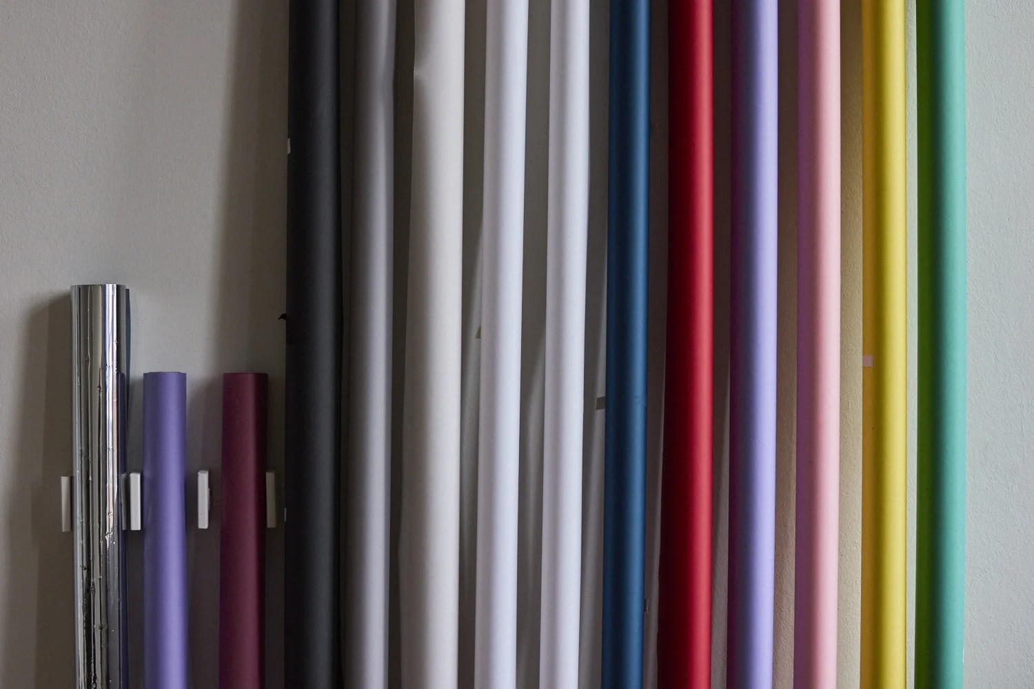 Colorful rolls of paper or fabric standing vertically against a wall.