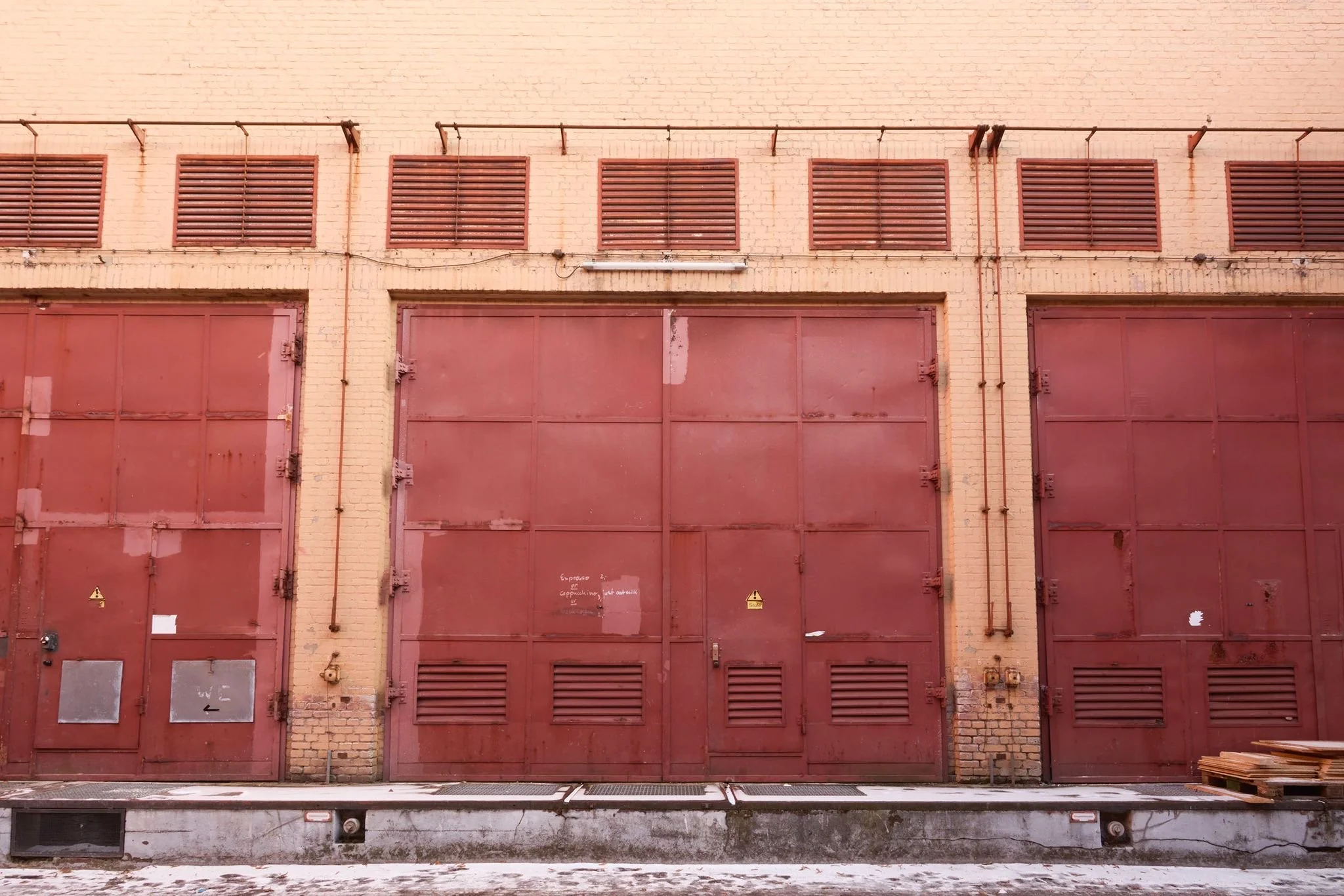 A brown brick building with multiple red metal garage doors and brown window shutters.