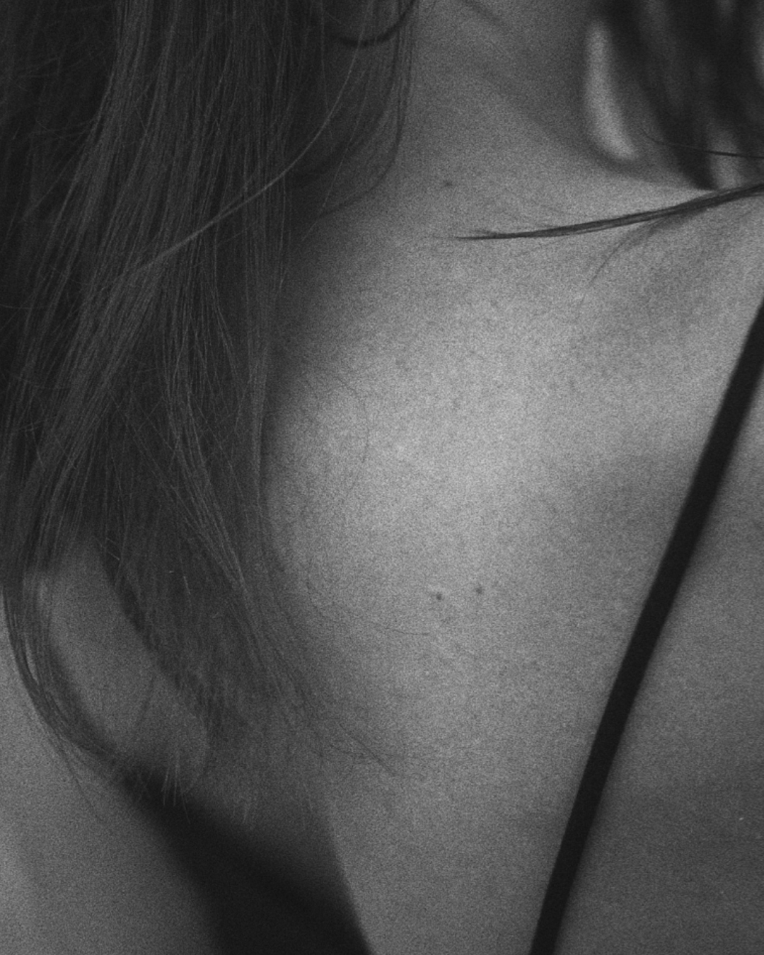 Close-up black and white photograph of a person's ear, hair, and part of their neck with a headphone cable visible.