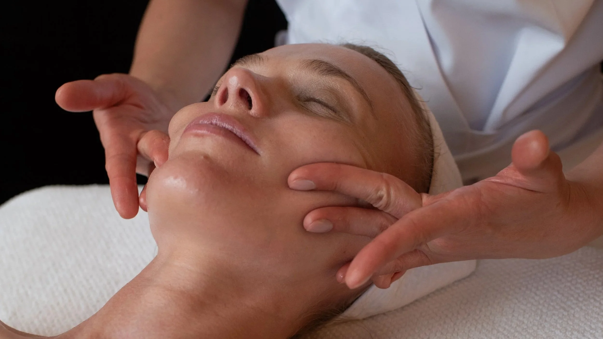 A woman receiving a facial treatment in a spa or clinic, lying on a treatment bed with a medical professional applying skincare product.