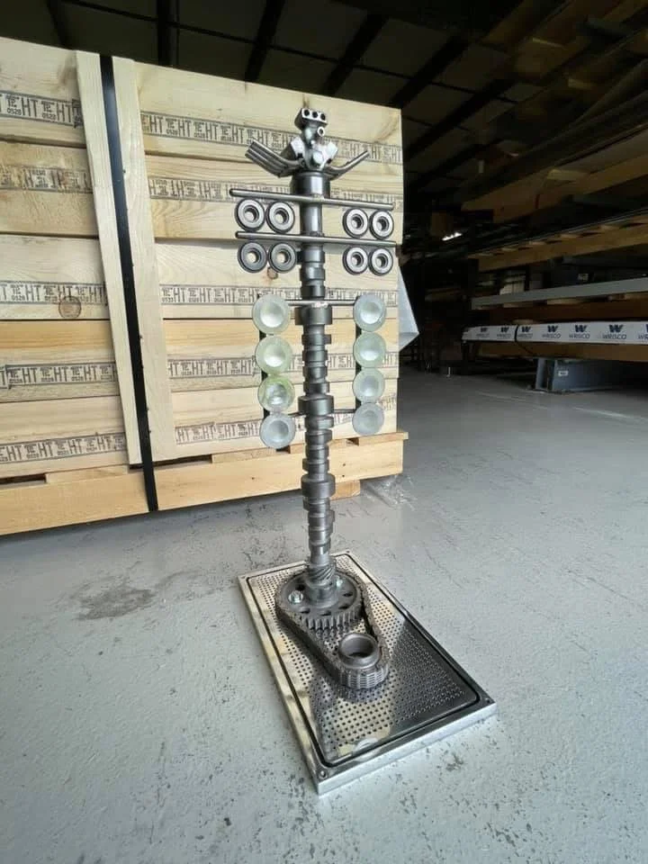 An artistic sculpture made from various mechanical parts standing on a platform in a warehouse.