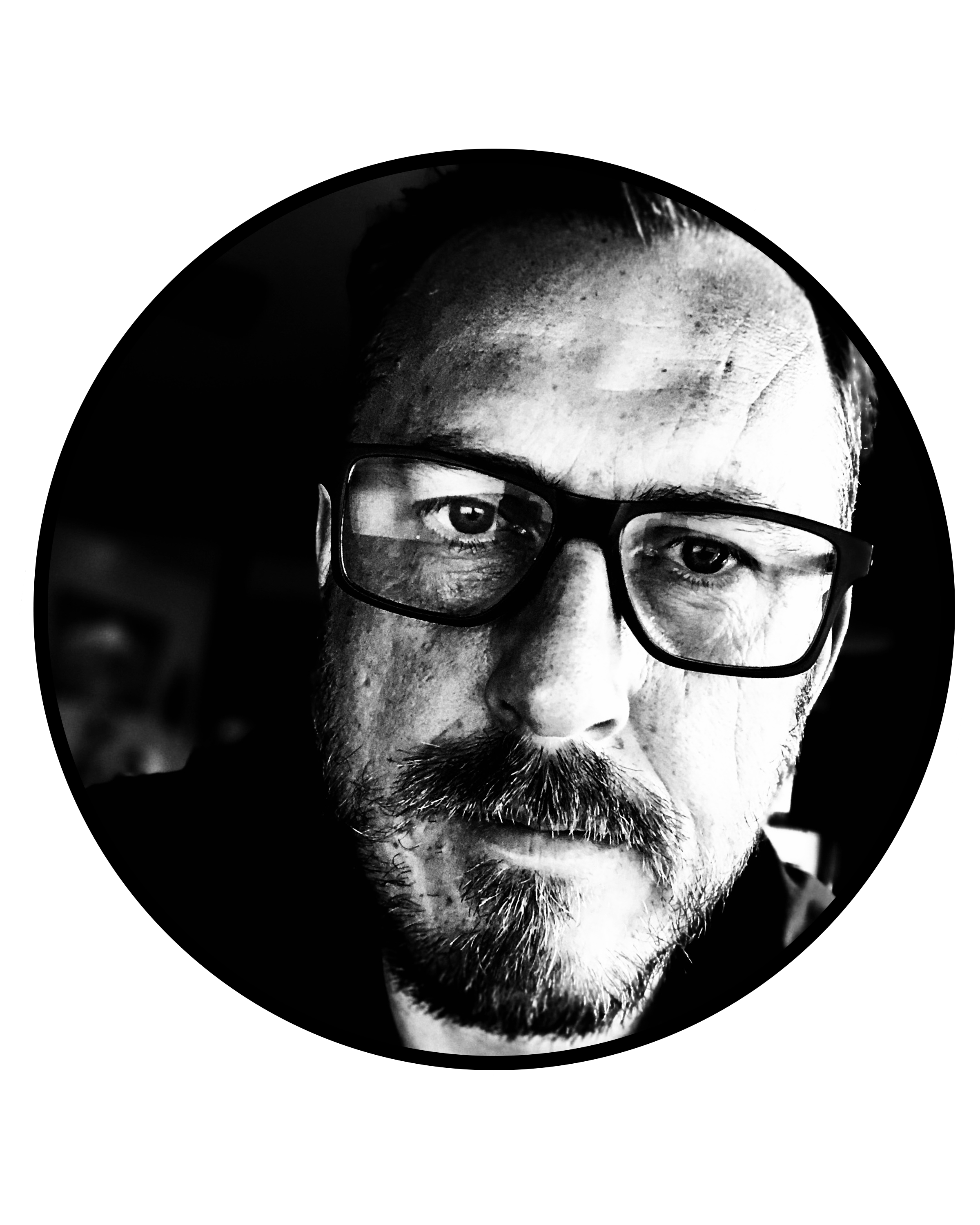 A black and white close-up portrait of a man with glasses, facial hair, and expressive eyes.