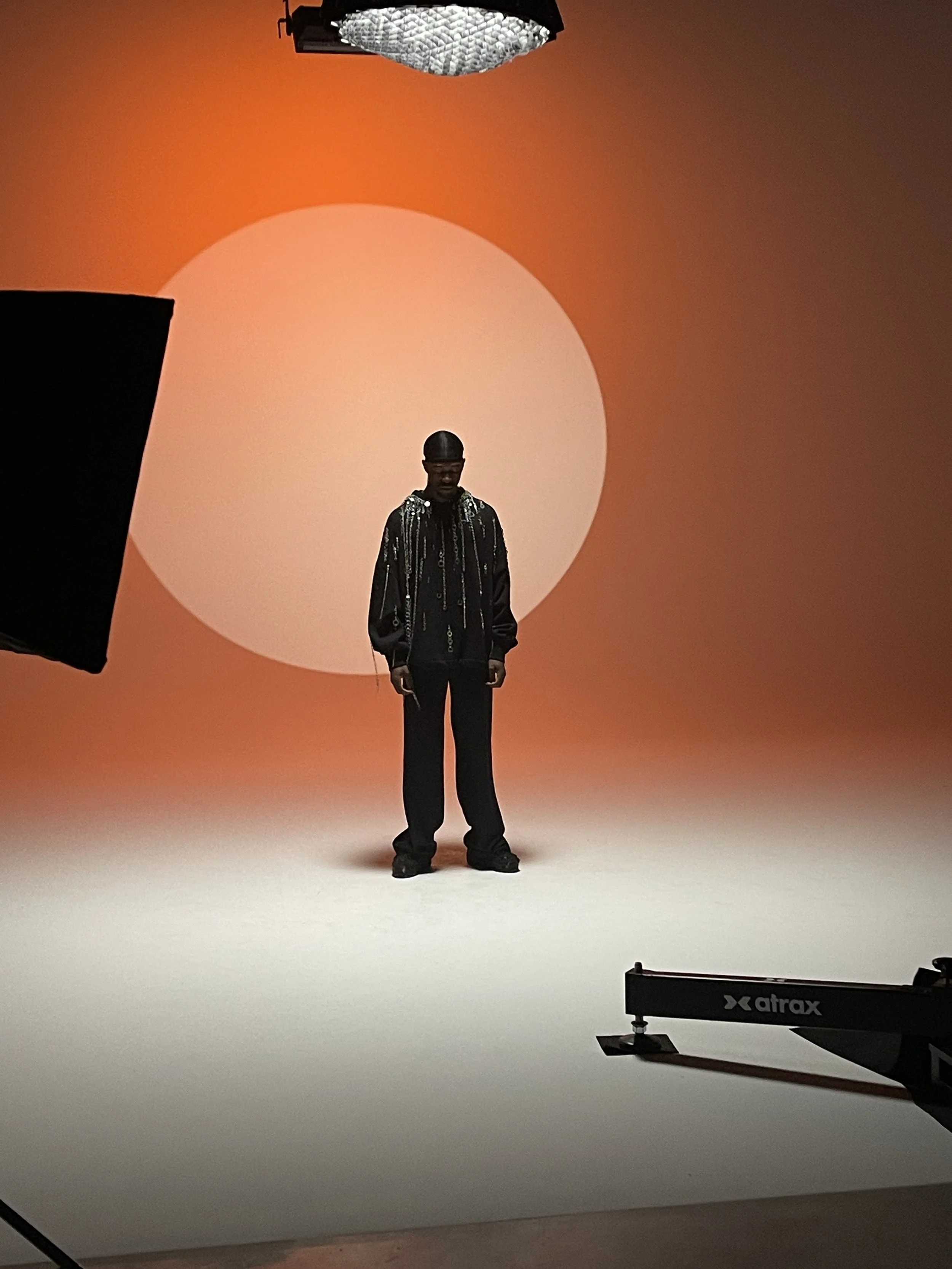 Une personne debout devant un fond orange avec un grand cercle clair, dans un studio de photographie.