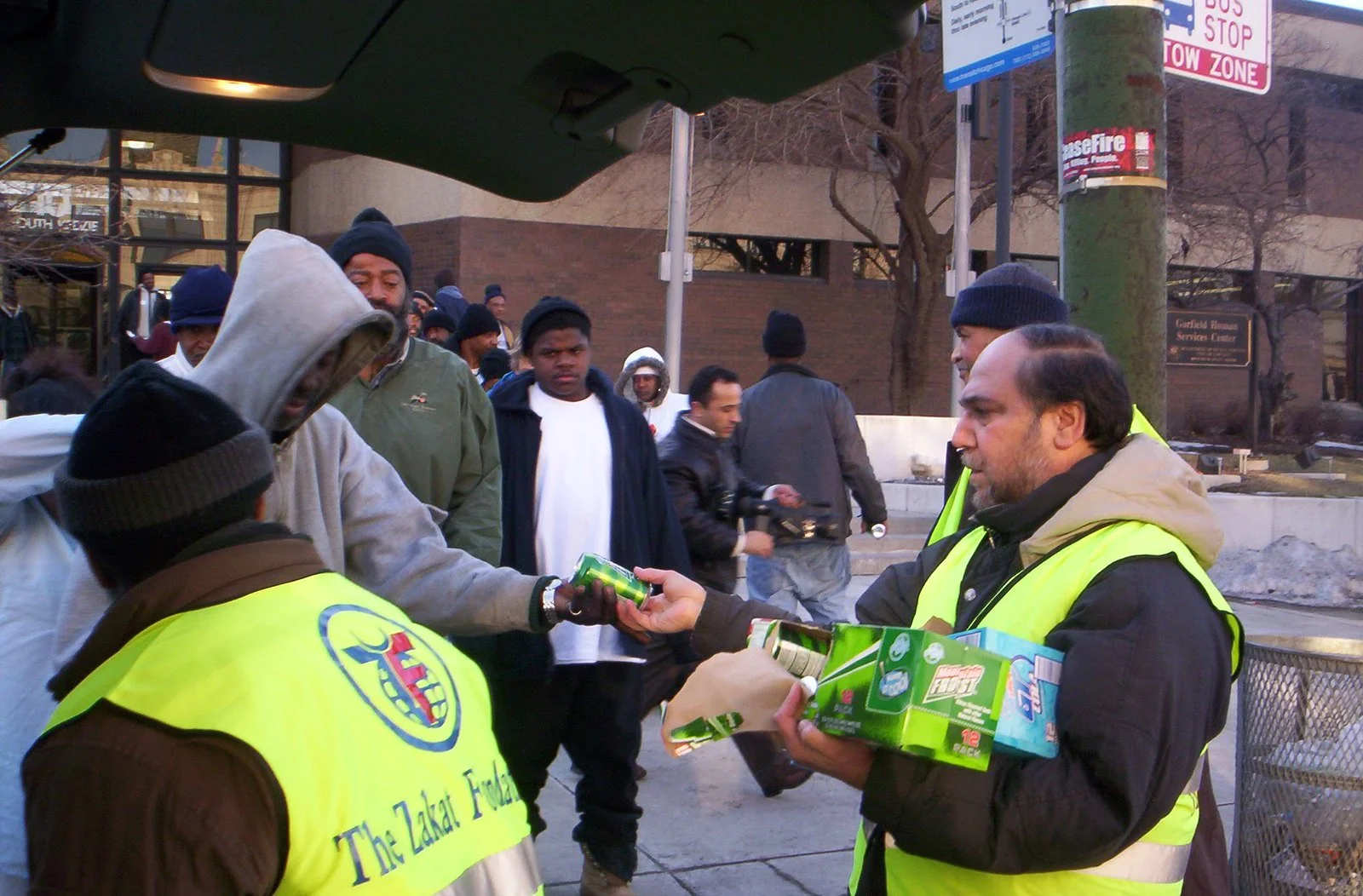 People in winter clothing exchange food and drinks on a city street.