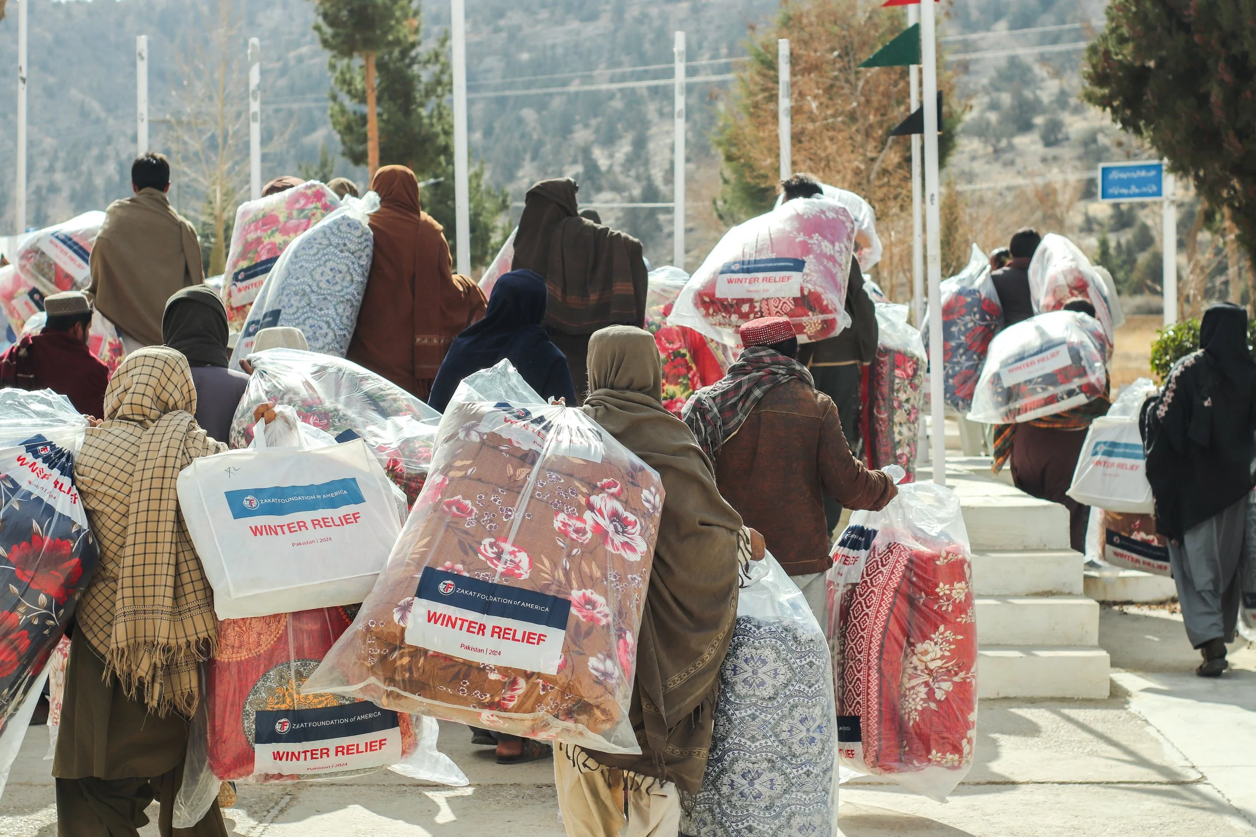 People carrying large sacks labeled 'Winter Relief' during a winter aid distribution event outdoors.