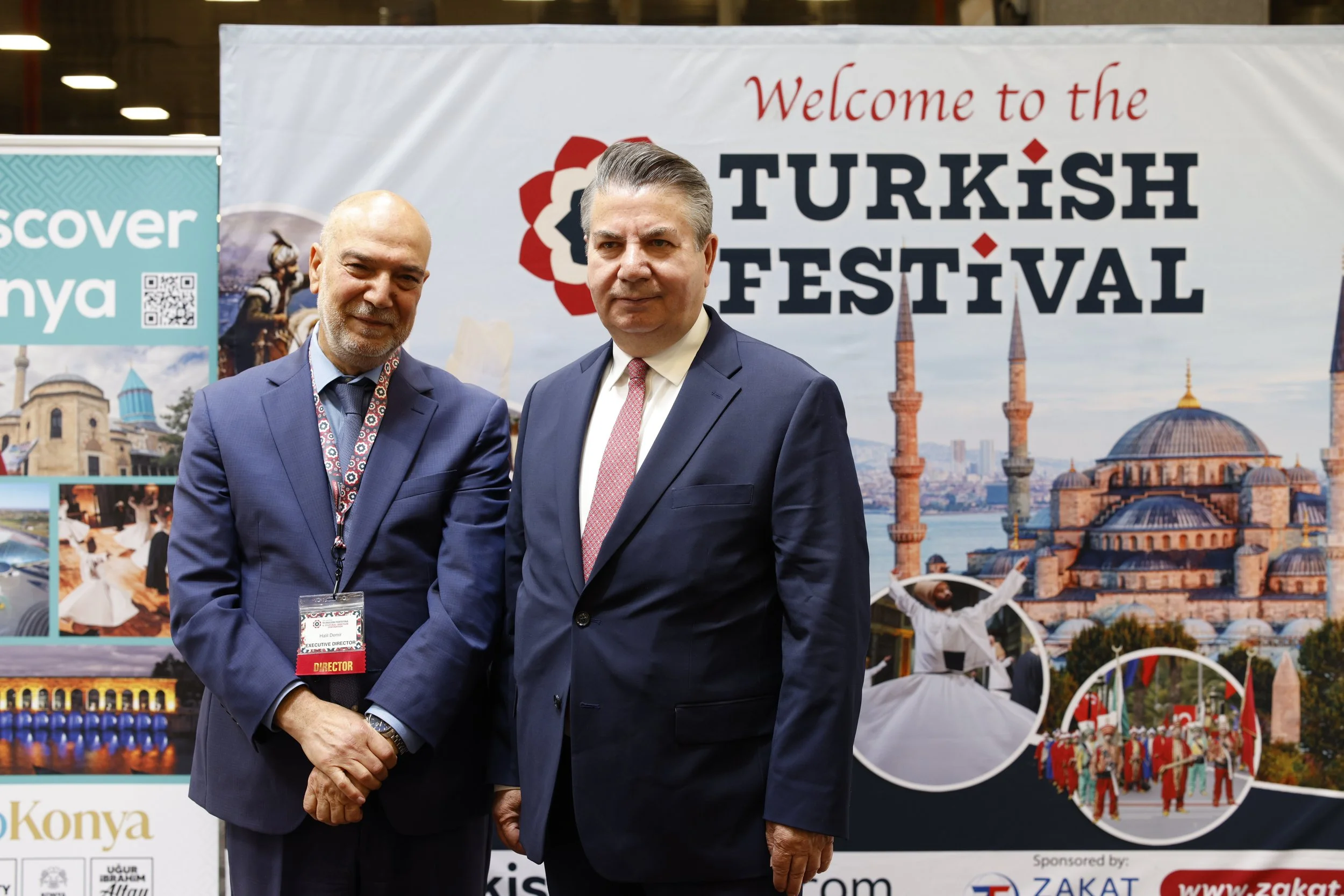 Two men in suits are standing in front of a banner that reads 'Welcome to the Turkish Festival.' The background features images of Turkish architecture, a mosque, and people in traditional clothing.
