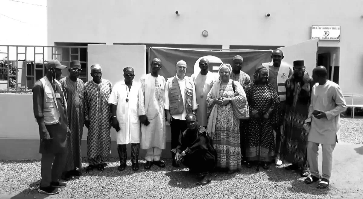 Group of people standing in front of a building with a flag hanging behind them.