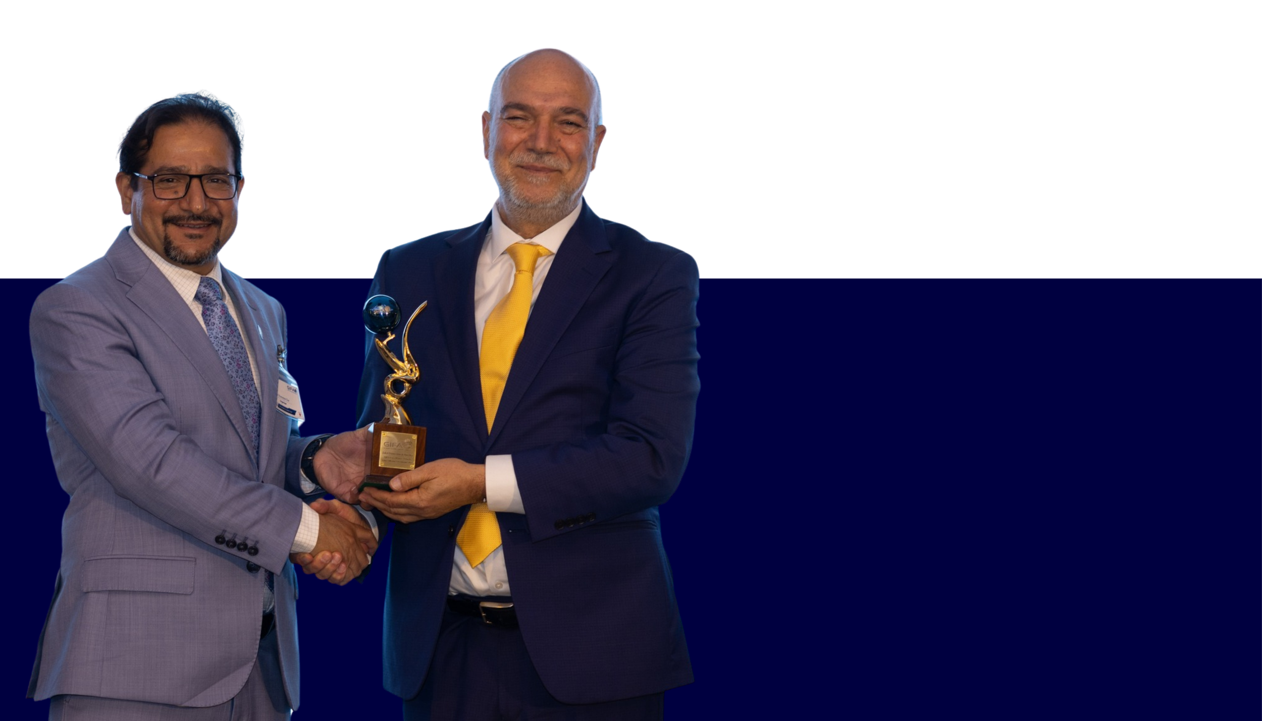 Two men, dressed in business suits, exchanging a trophy and shaking hands at an award ceremony, with a white and dark blue background.
