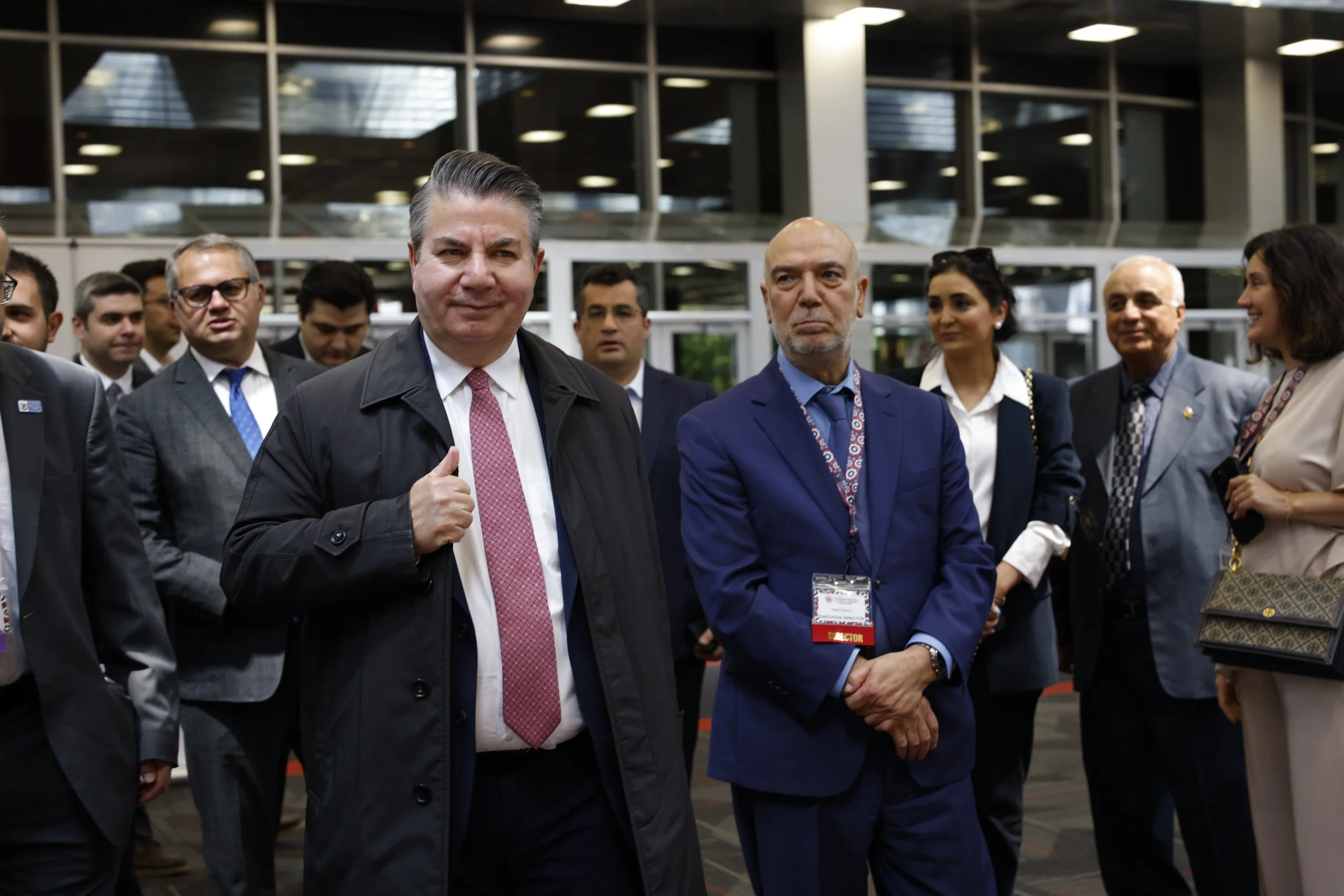 Group of people in formal attire gathered at the Turkish Festival with two men in the foreground, one giving a thumbs-up.