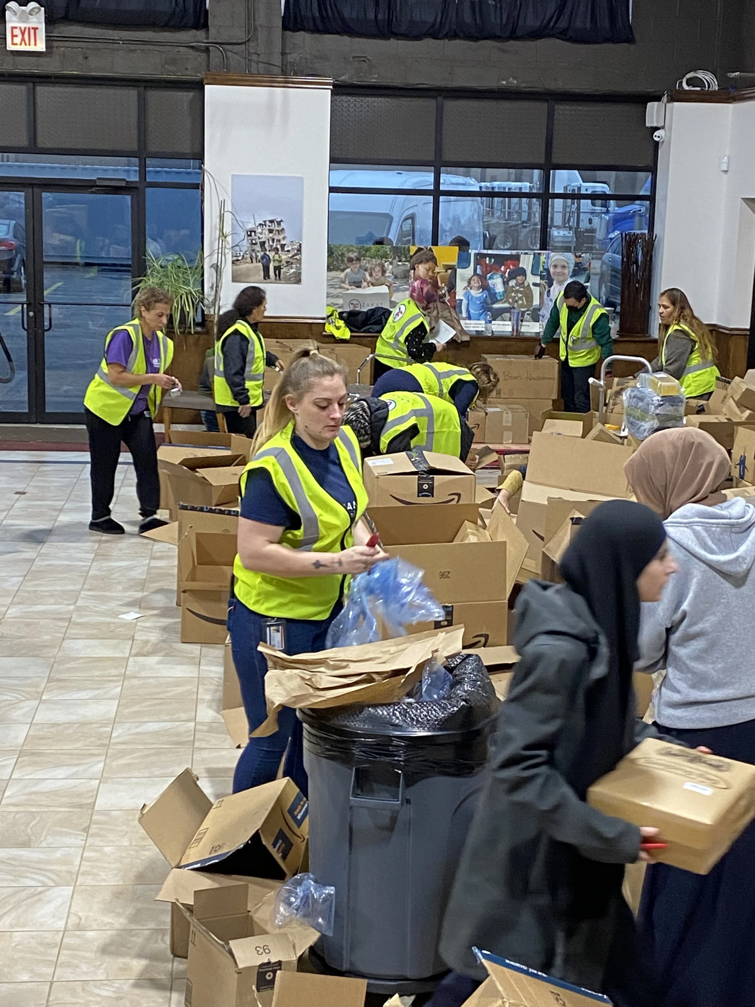 People working together to pack boxes in a store or warehouse, with boxes and trash bins around.