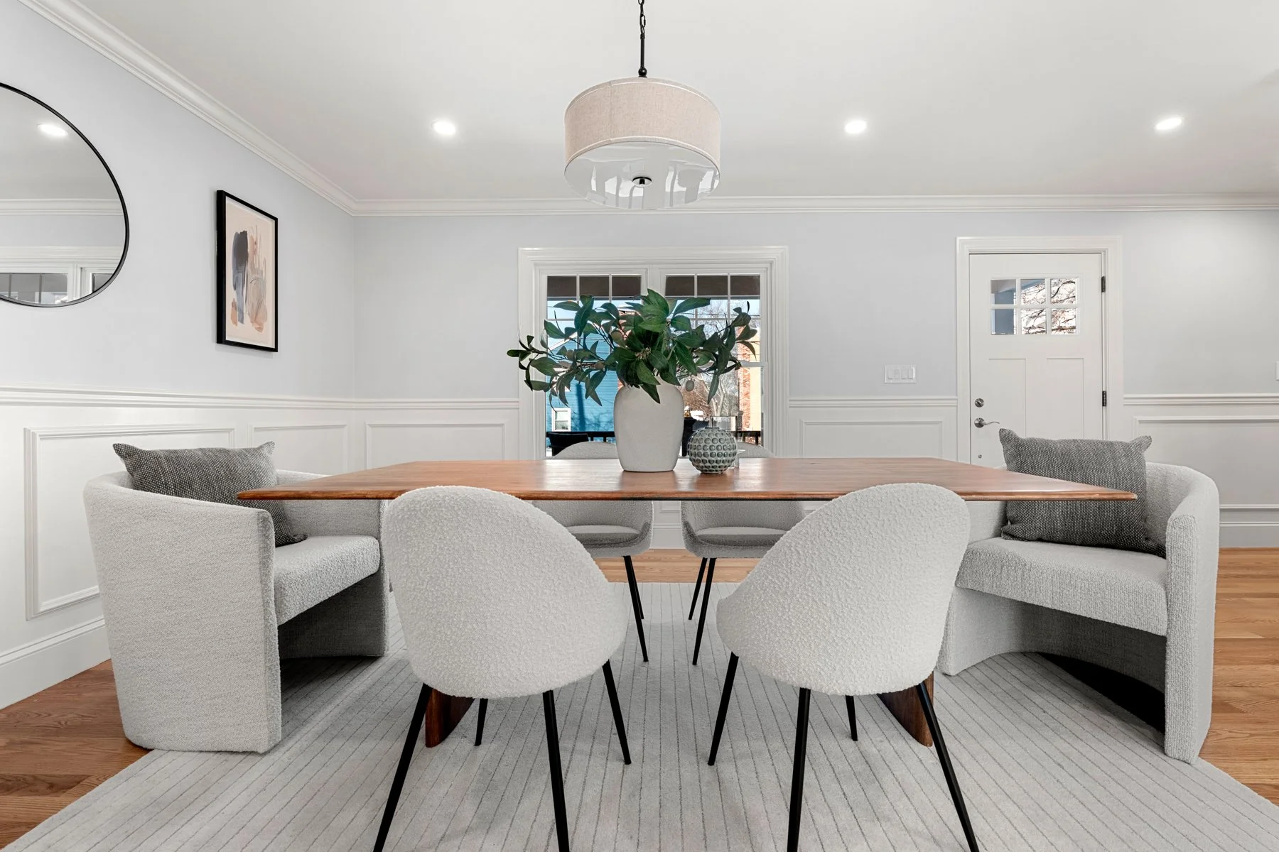 Bright enclosed porch with large windows, white walls and ceiling, brick and wooden exterior, small sofa with pillows, potted plant, and area rug.
