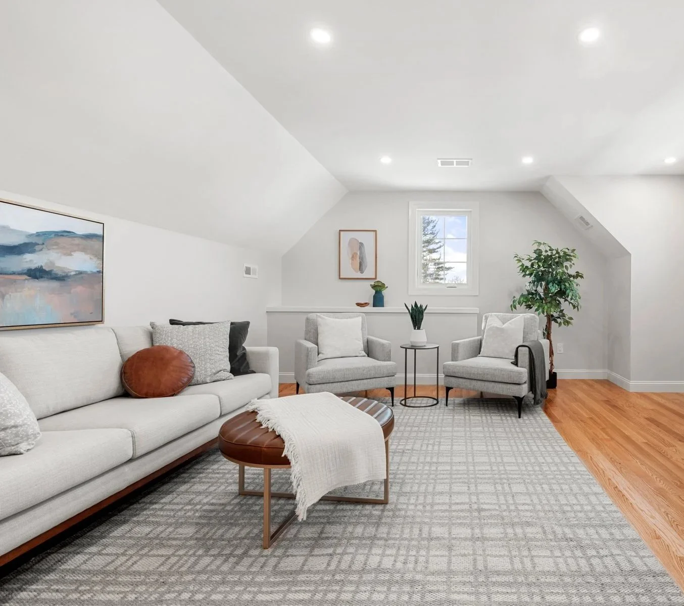 Living room with white walls, large windows, two white armchairs with gold accents, a beige area rug, a black table with a lamp, a large abstract painting, a potted plant, and a small side table with a plant.