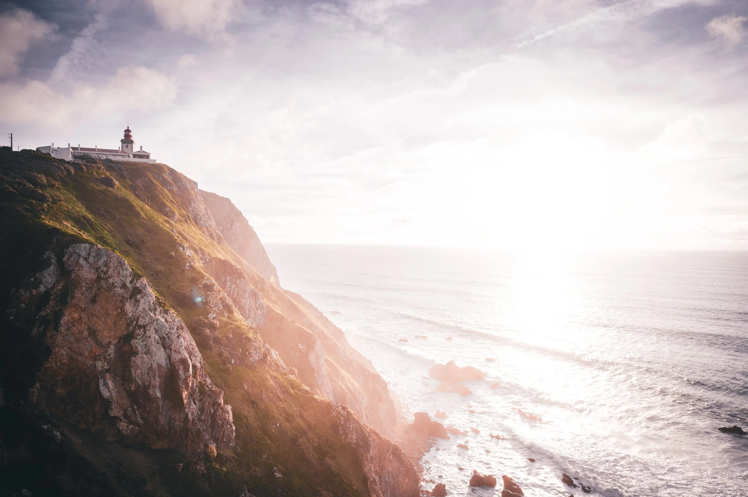 Klippen an der Küste mit Leuchtturm auf dem höchsten Punkt, Sonnenlicht, Meer und Himmel im Hintergrund