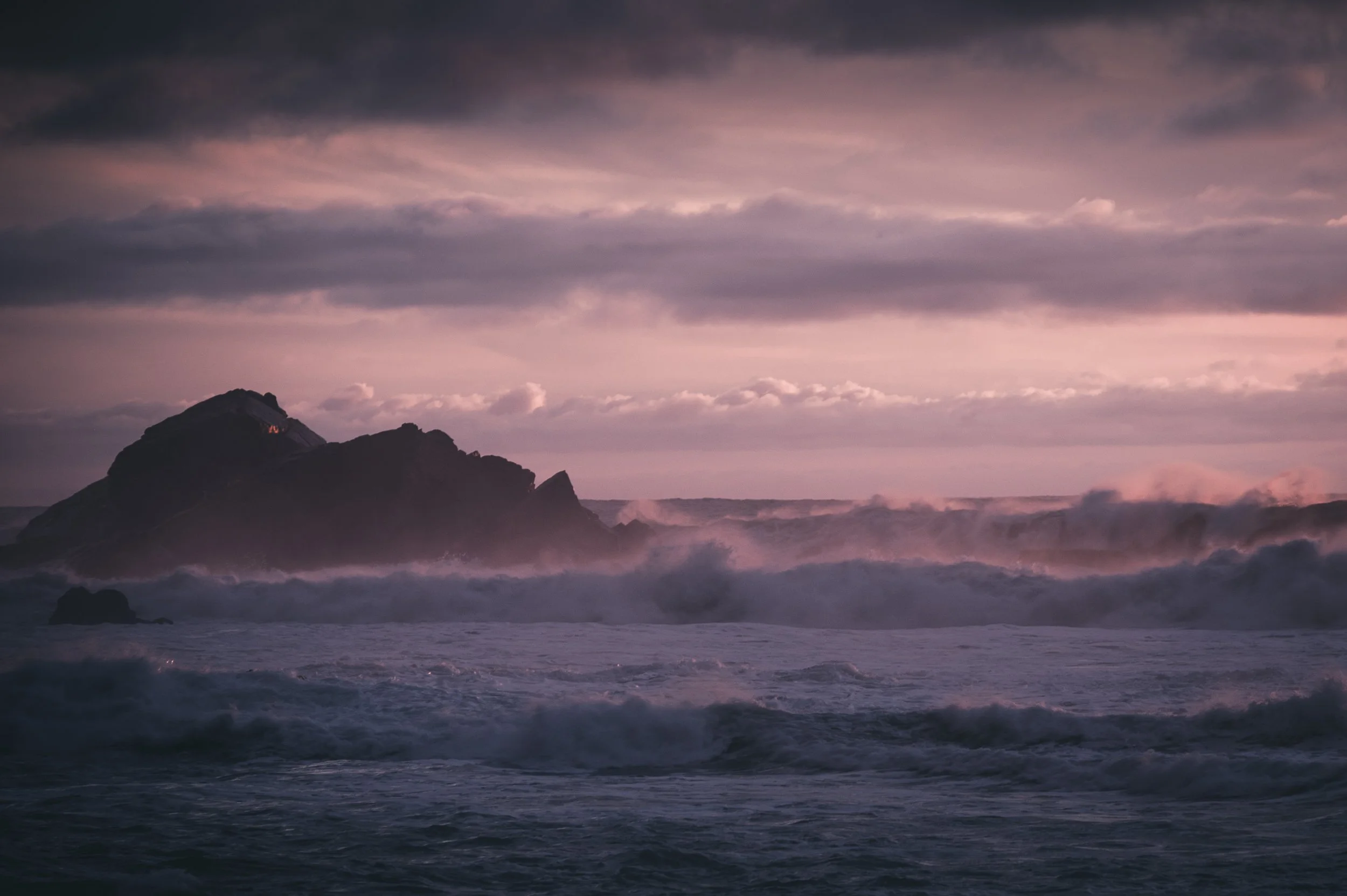Sturm auf dem Meer mit großen Wellen, dunkle Wolken am Himmel und eine große Felseninsel im Hintergrund.