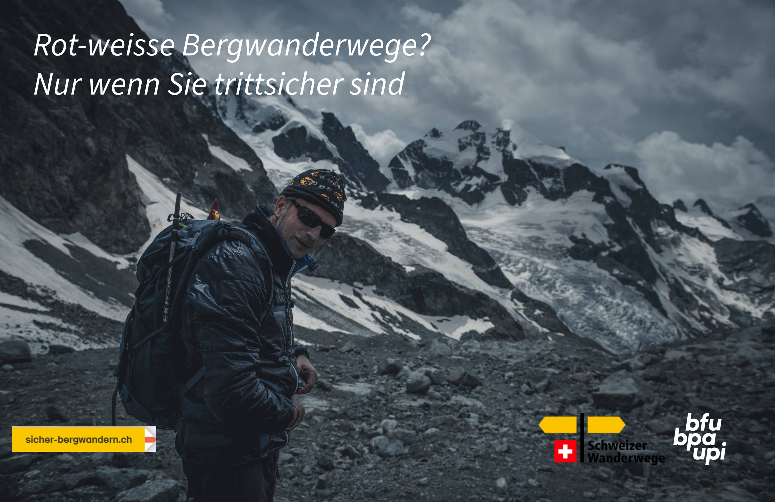 Ein Mann in dunkler Outdoor-Bekleidung mit Rucksack steht in einer Gebirgslandschaft mit schneebedeckten Gipfeln und Steinen. Über dem Bild schwarzer Himmel mit Wolken, Text auf Deutsch, abwärts rechte Ecke Logos der Schweizer Wanderwege, Schweizer F