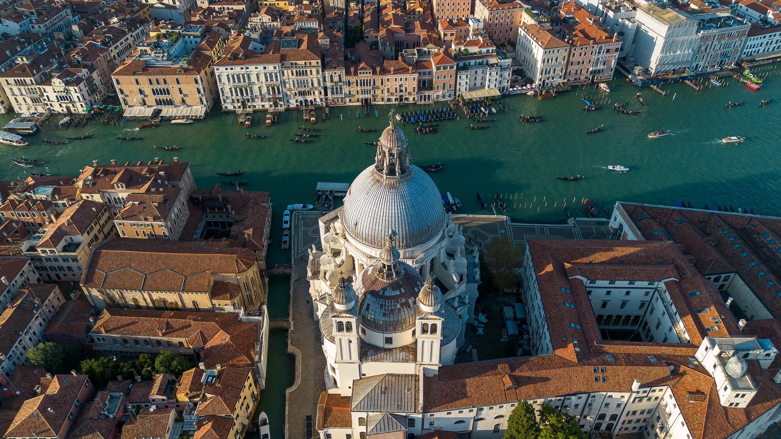 Luftaufnahme der Basilika Santa Maria della Salute in Venedig, umgeben von Wasser und historischen Gebäuden mit roten Ziegeldächern.