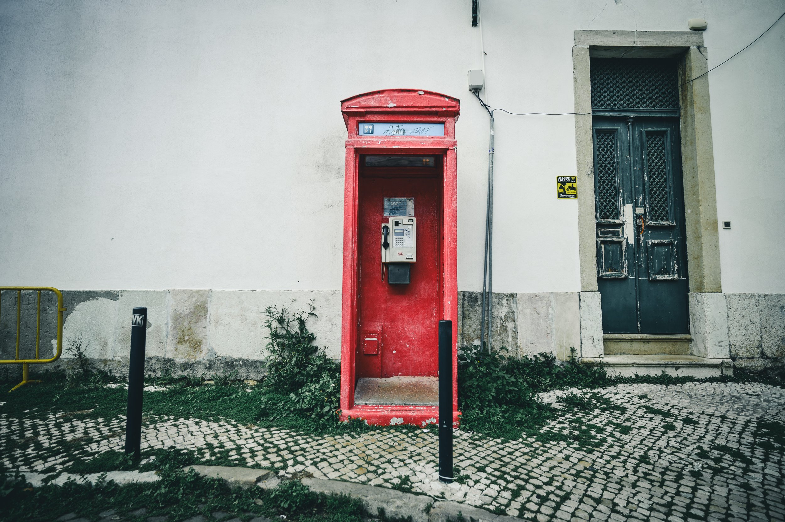 Altes rotes Telefonhäuschen neben einem schwarzen Tür und einer weißen Wand