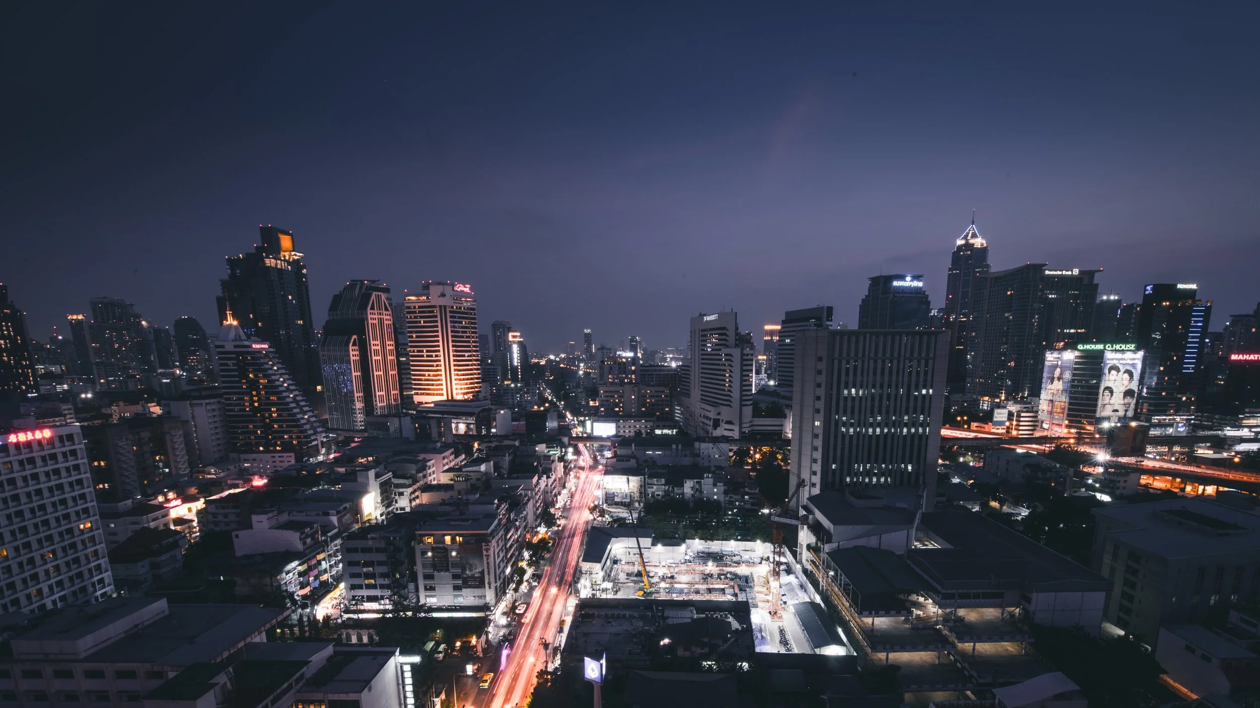 Nachtsicht auf eine moderne Stadt mit Wolkenkratzern, beleuchteten Gebäuden und beleuchteter Straße mit vorbeiziehenden Autos.