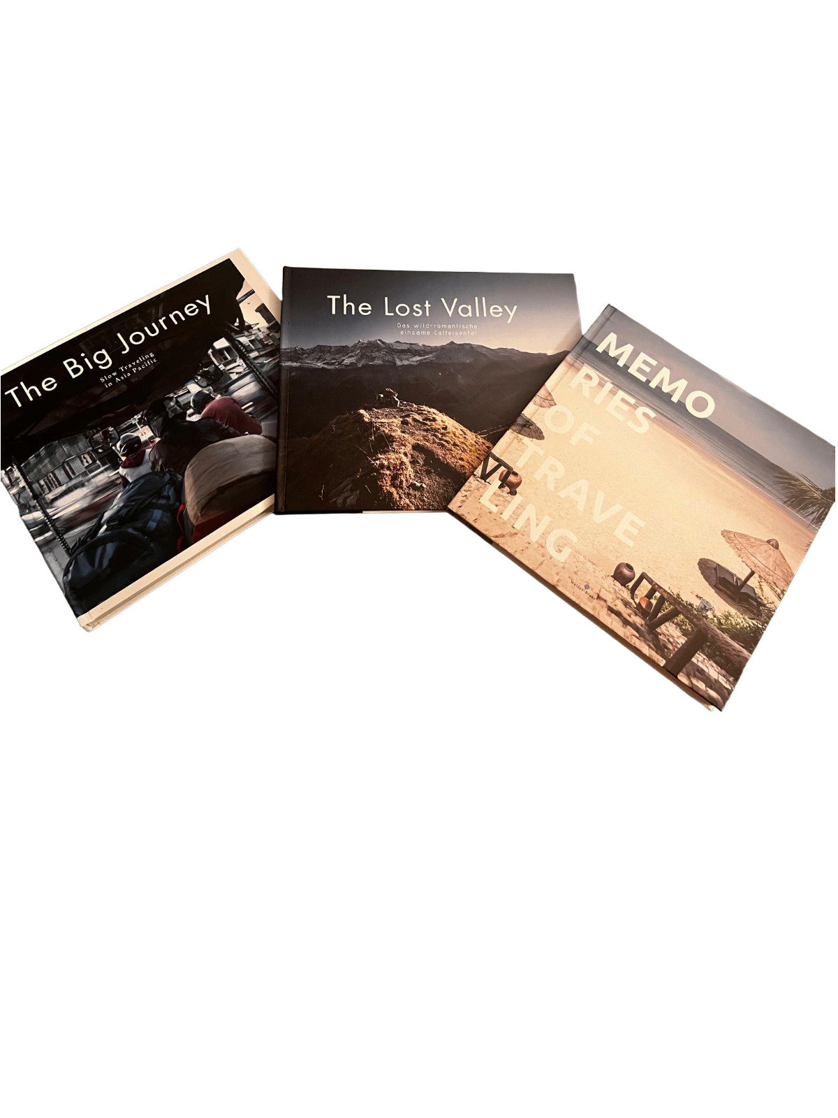 Drei aufgeschlagene Fotobücher mit Titeln: 'The Big Journey', 'The Lost Valley' und 'Memo Rie of Travel Living' auf schwarzem Hintergrund.