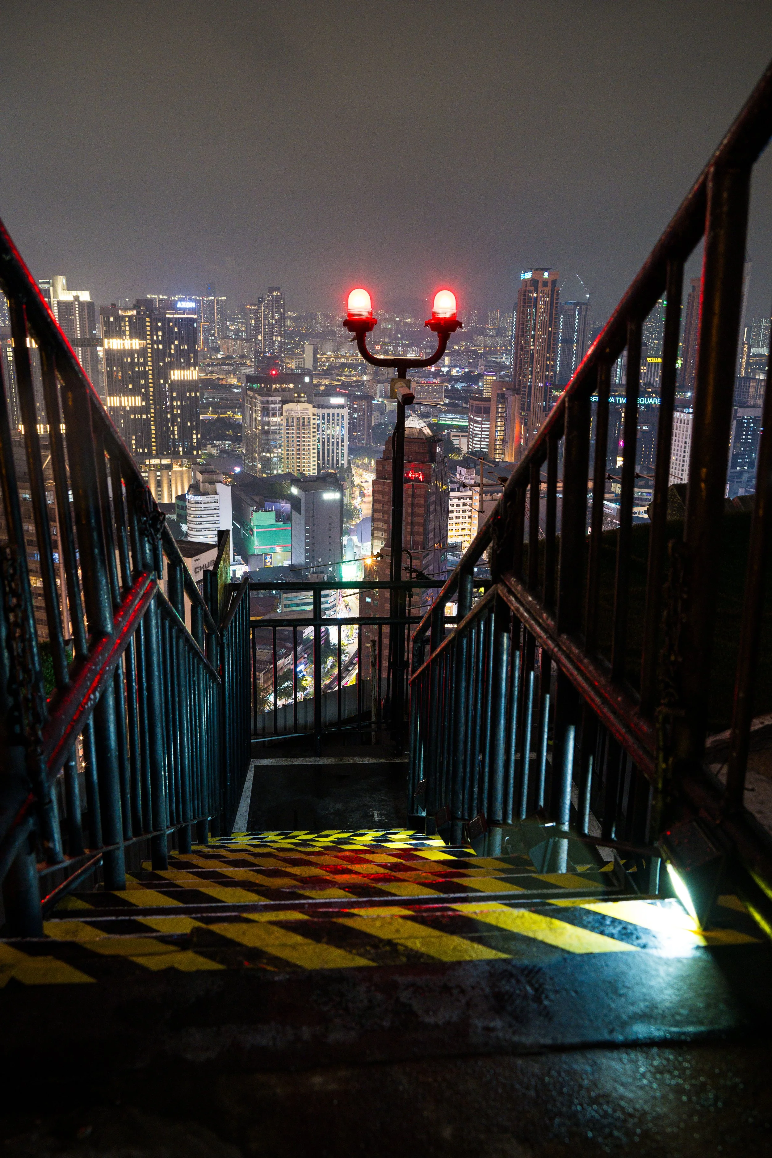Ausblick von einem hohen Gebäude bei Nacht mit Stadtlaterne und beleuchteter Skyline im Hintergrund.