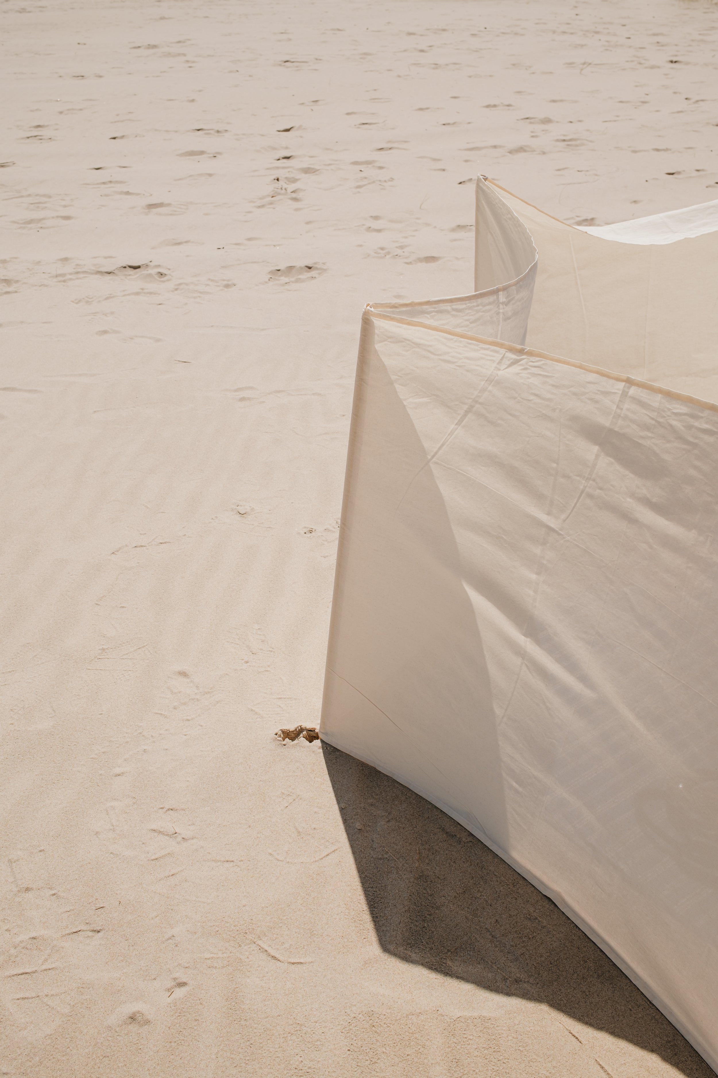 Close-up of fabric that appears to be beach windbreakers, on a sandy beach.