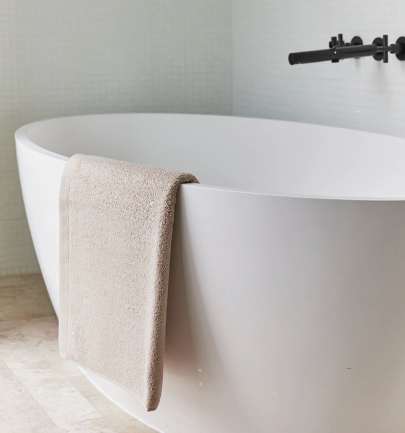 Clawfoot bathtub in a bathroom with a towel draped over the side and a mounted black faucet.