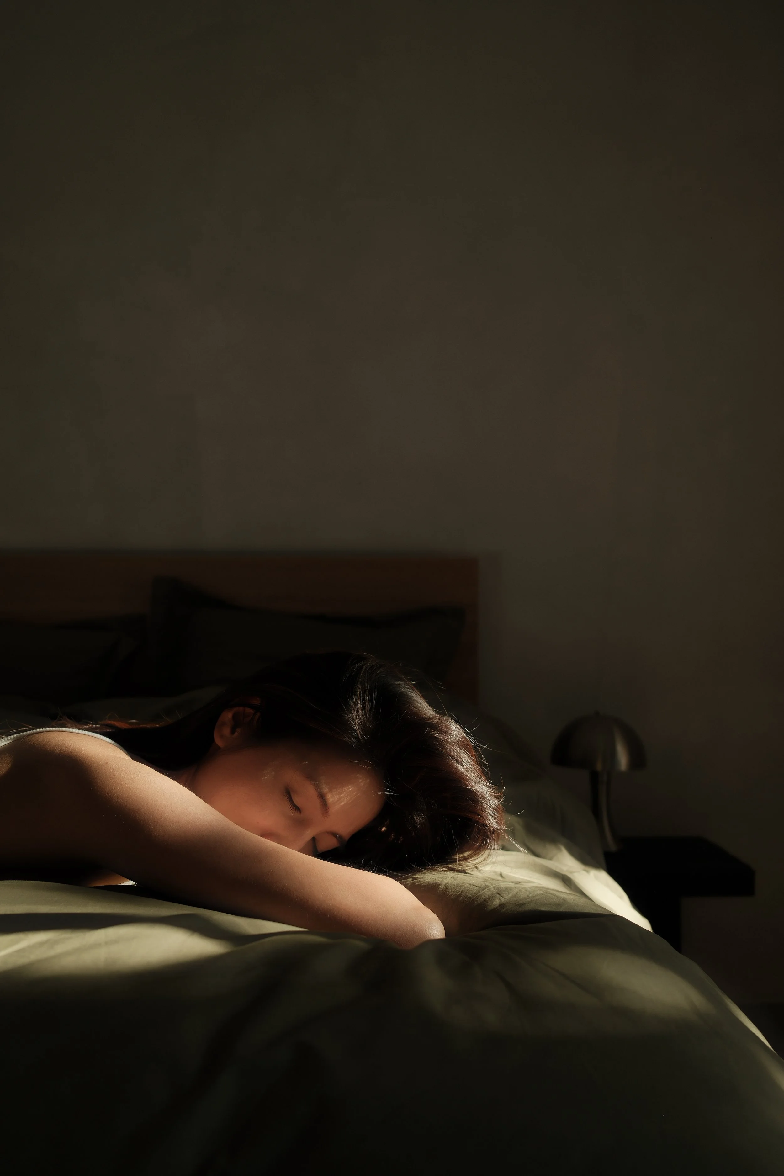 A woman sleeping peacefully in a darkened bedroom with minimal lighting, lying on her side with her head on a pillow.