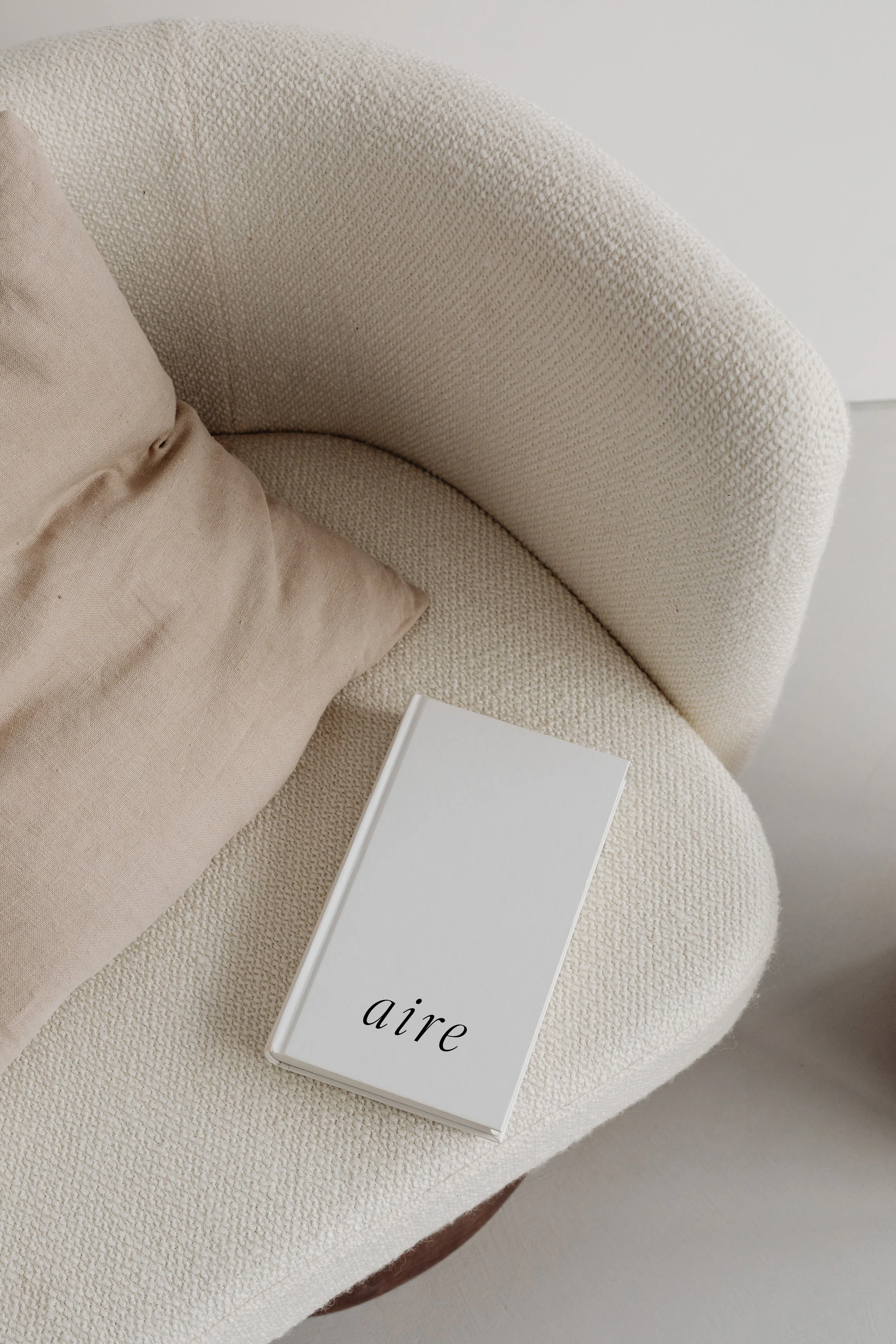 A beige textured armchair with a matching pillow and a white book titled 'aire' resting on the seat.