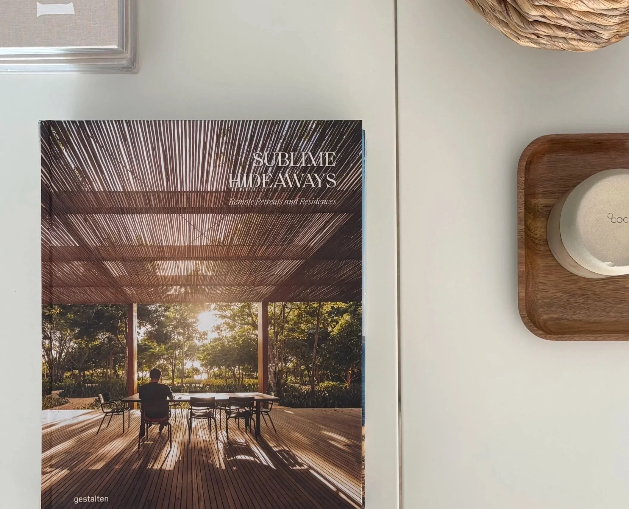 A magazine cover titled 'SUBLIME HIDEAWAYS' featuring a wooden pavilion with a slatted roof in a natural setting, with a person sitting at a table outdoors in sunlight.