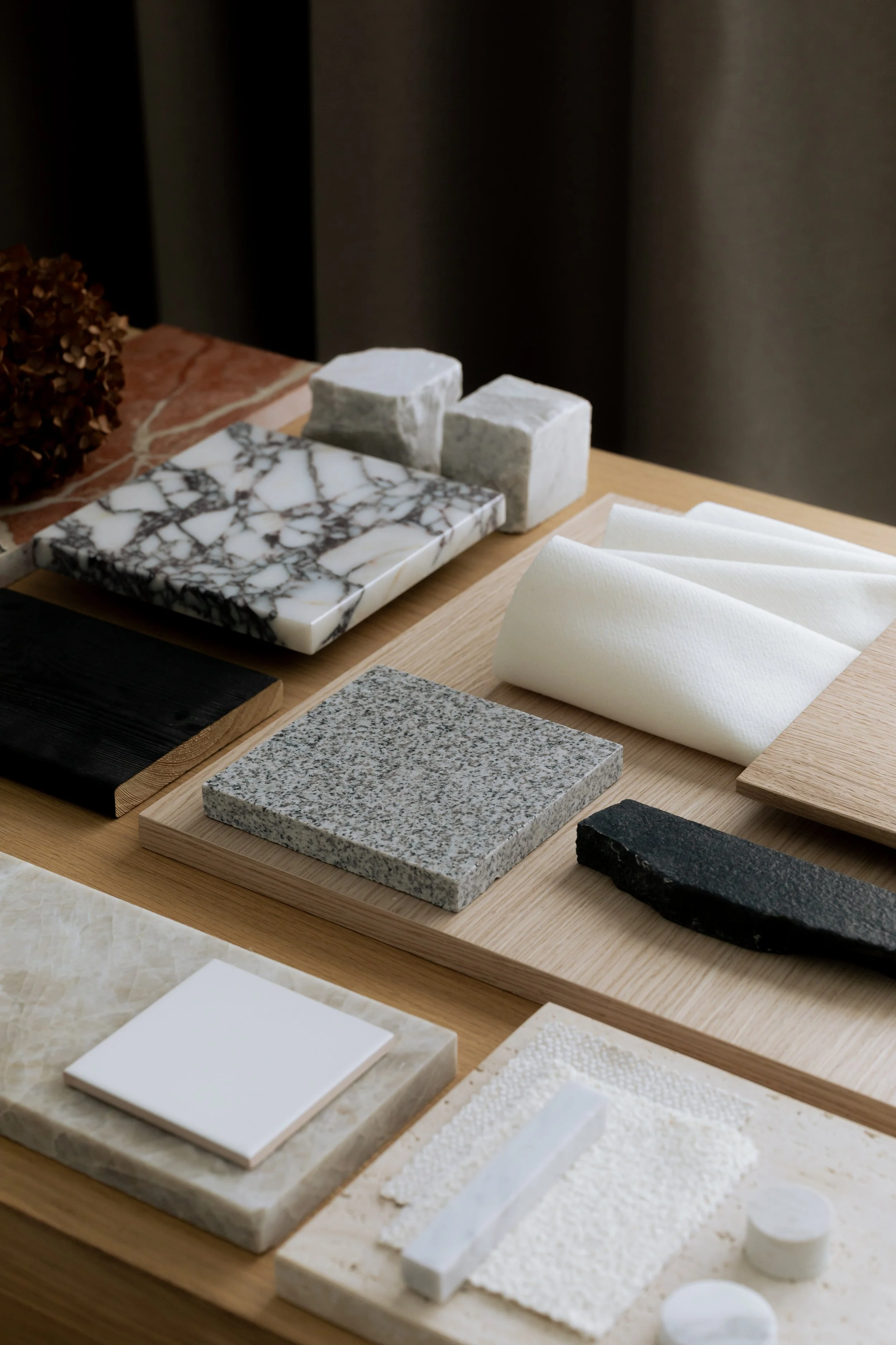 A collection of various tiles, stone samples, and swatches arranged on a wooden table, including marble, granite, and ceramic options for interior design.