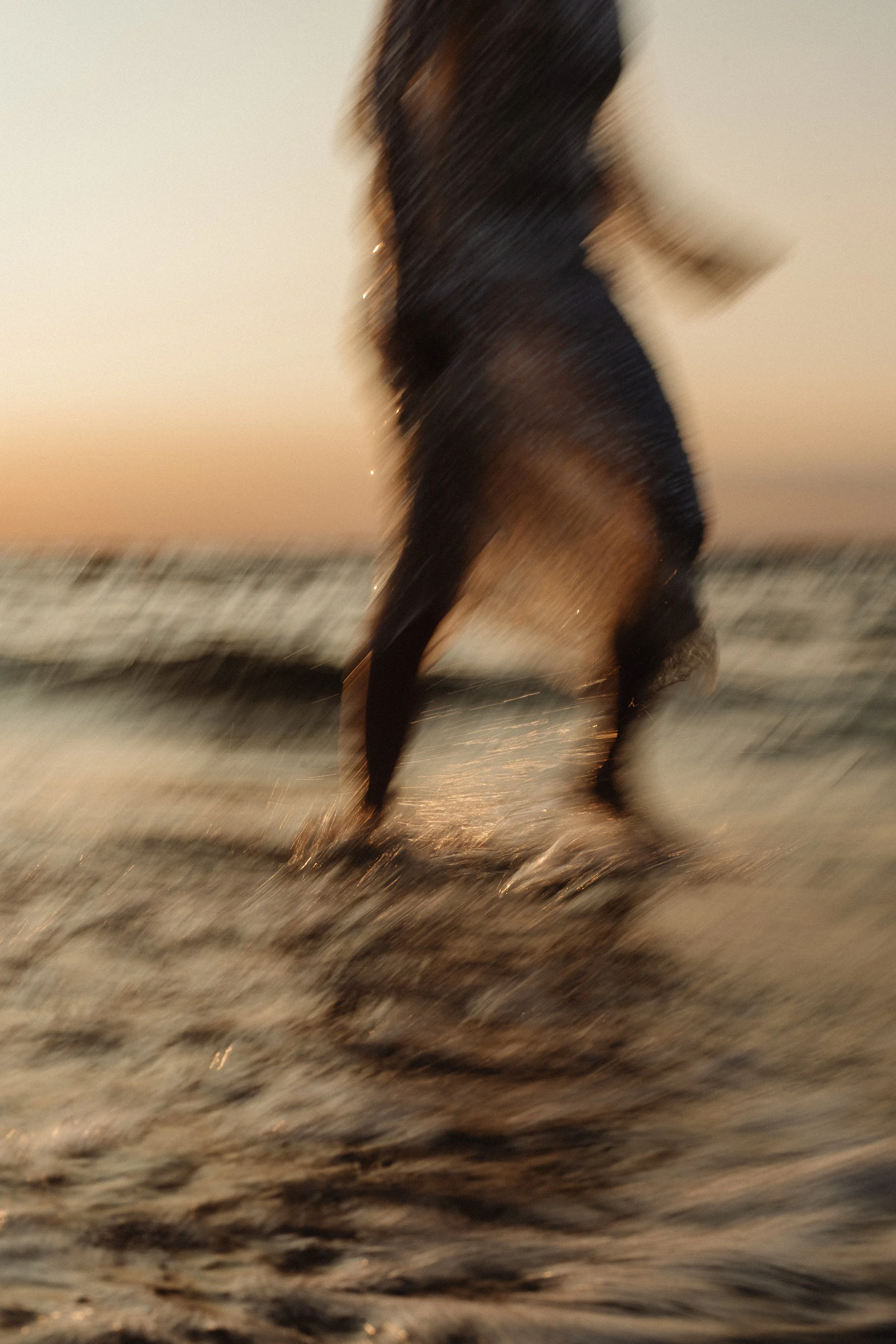 Blurred image of a person running through shallow water at sunset or sunrise on a beach.