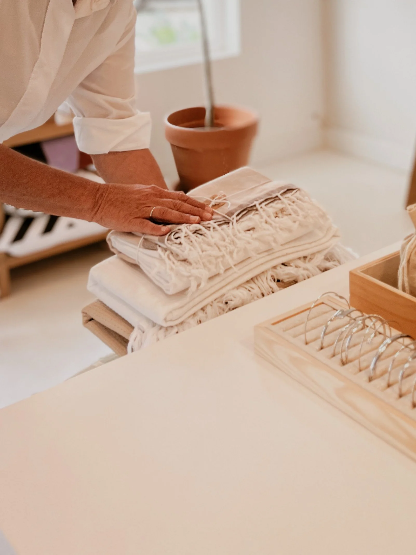 Person folding a beige cloth or textile on a white table in a bright room with natural light.