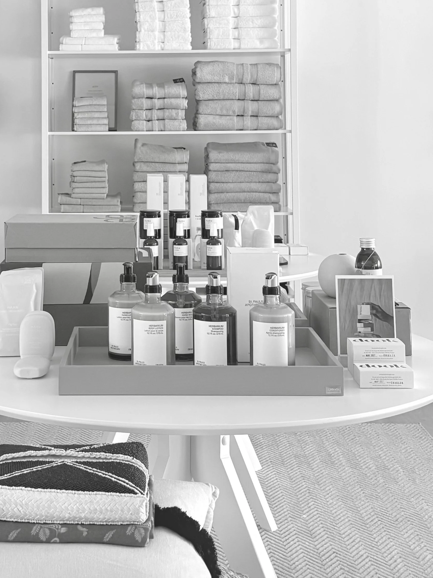 Display of folded towels, bottles, and boxes on a white table in a retail store, with a shelf of towels in the background.