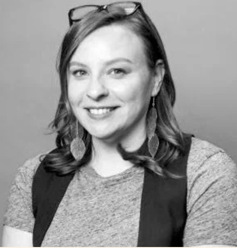 Black and white photo of a woman with glasses on her head, wearing earrings and a casual shirt, smiling at the camera.