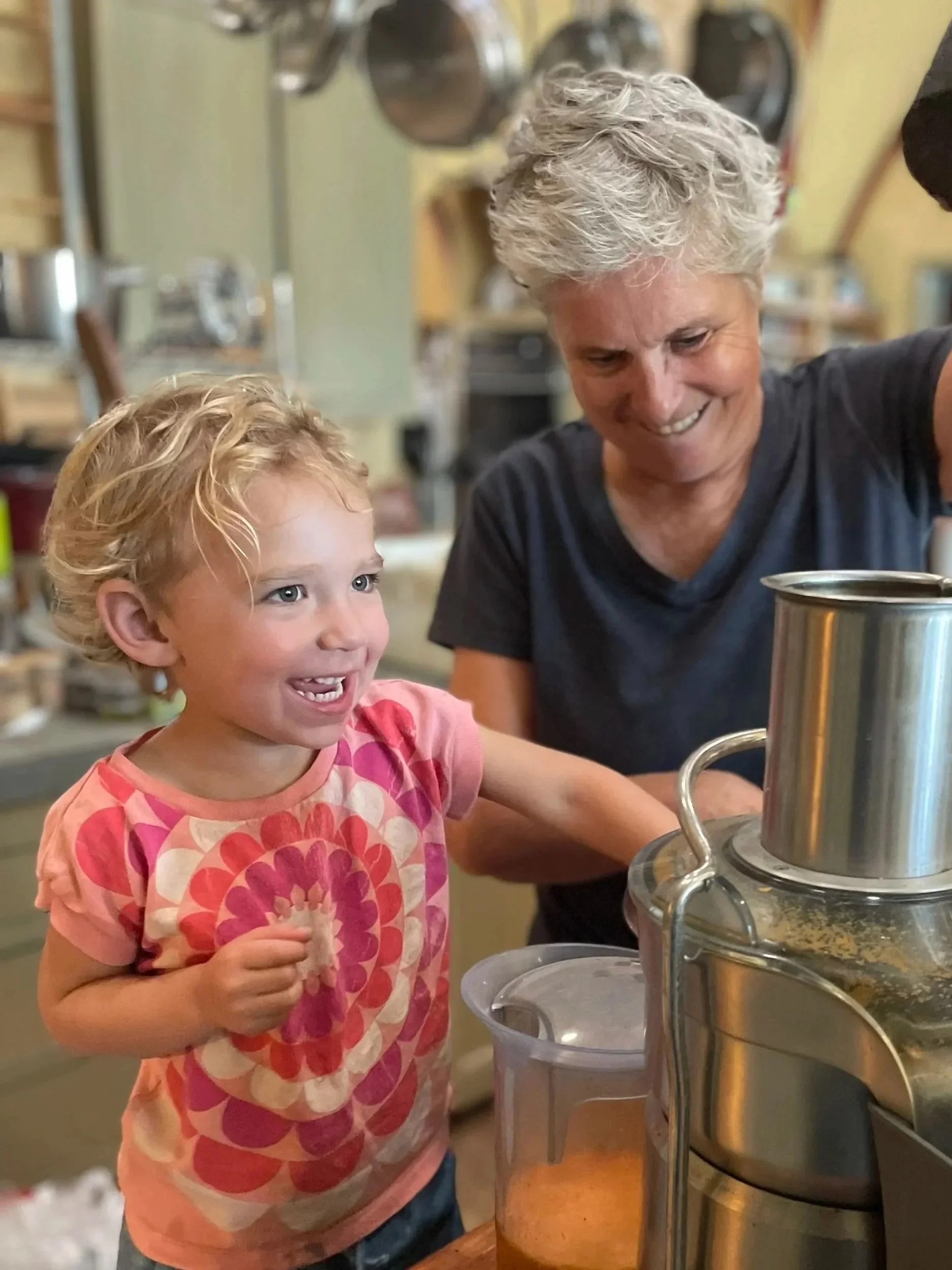A young girl and an older woman making juice using a juicer in a kitchen.