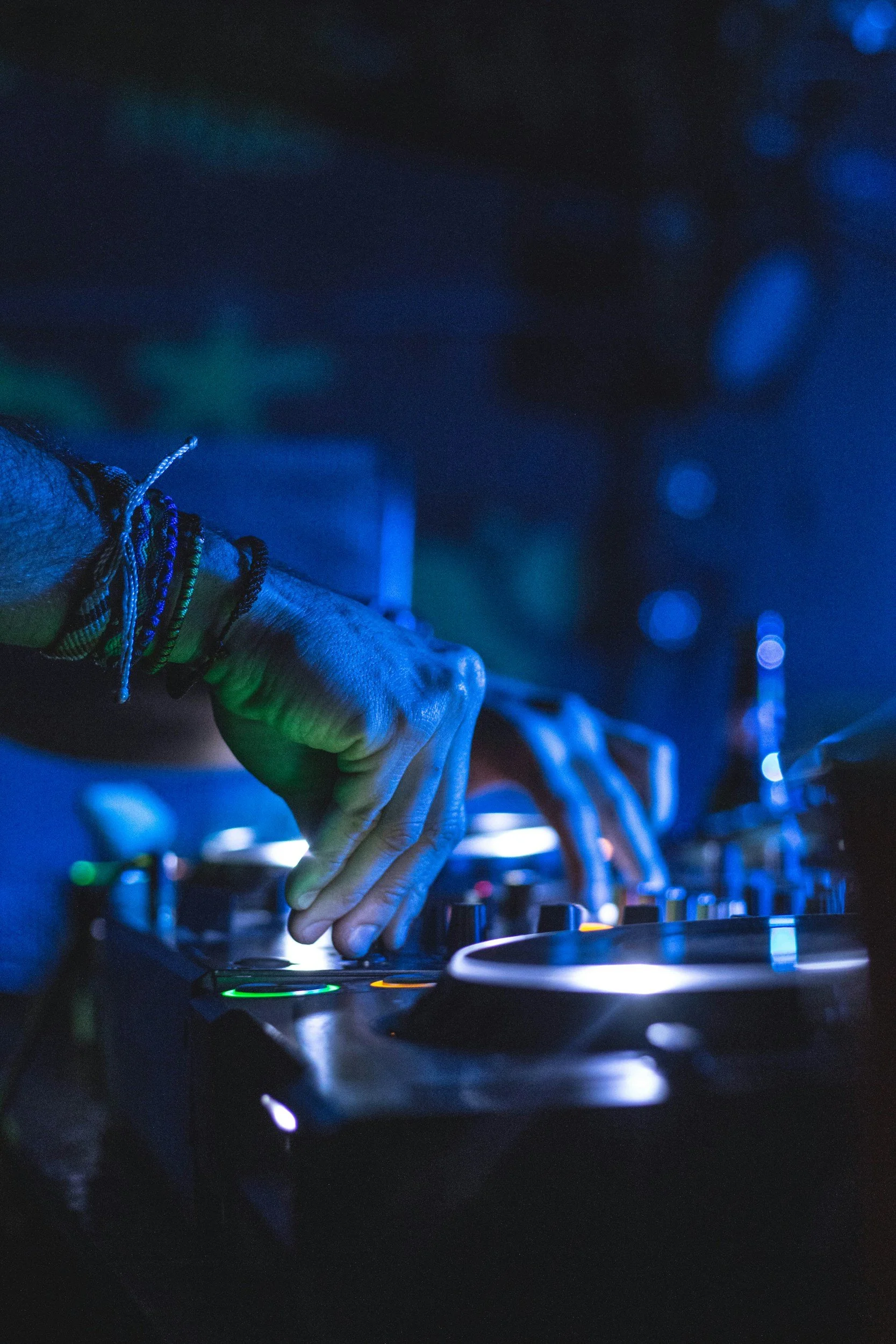 Close-up of a DJ's hand manipulating a mixer in a dark, blue-lit setting.