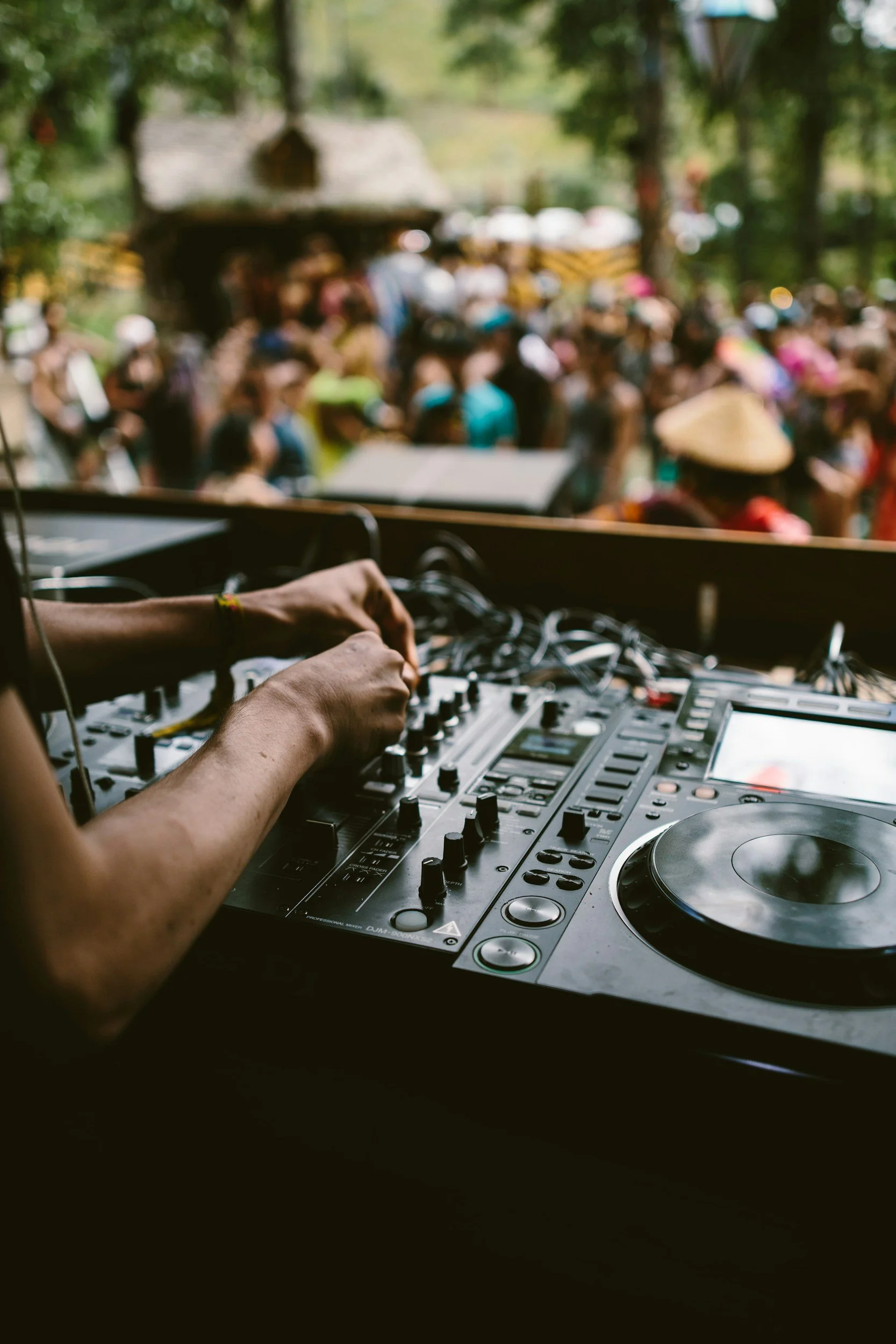 DJ playing music at outdoor festival with crowd in background.